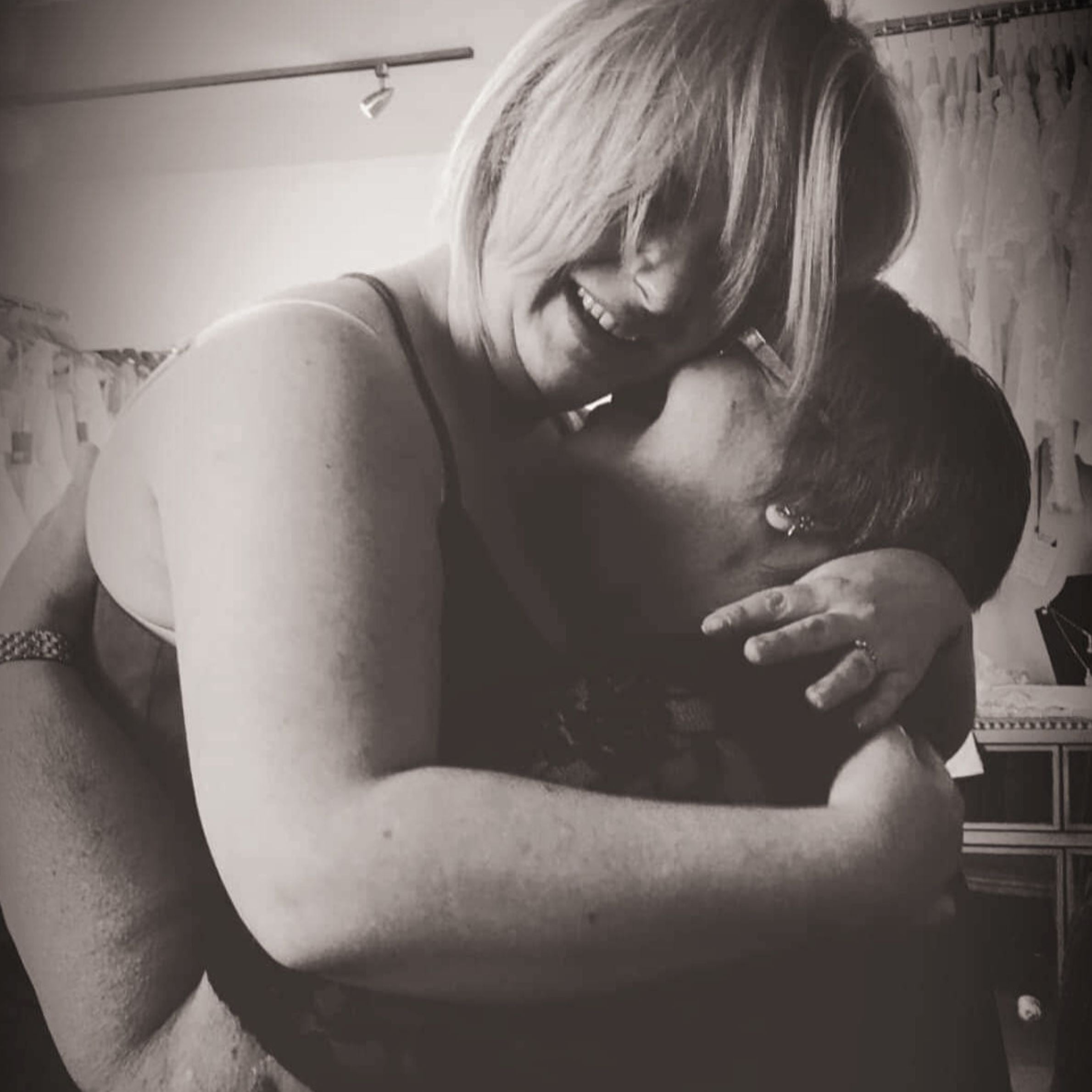 Black and white image of a blonde woman hugging a woman with brown hair. They are smiling