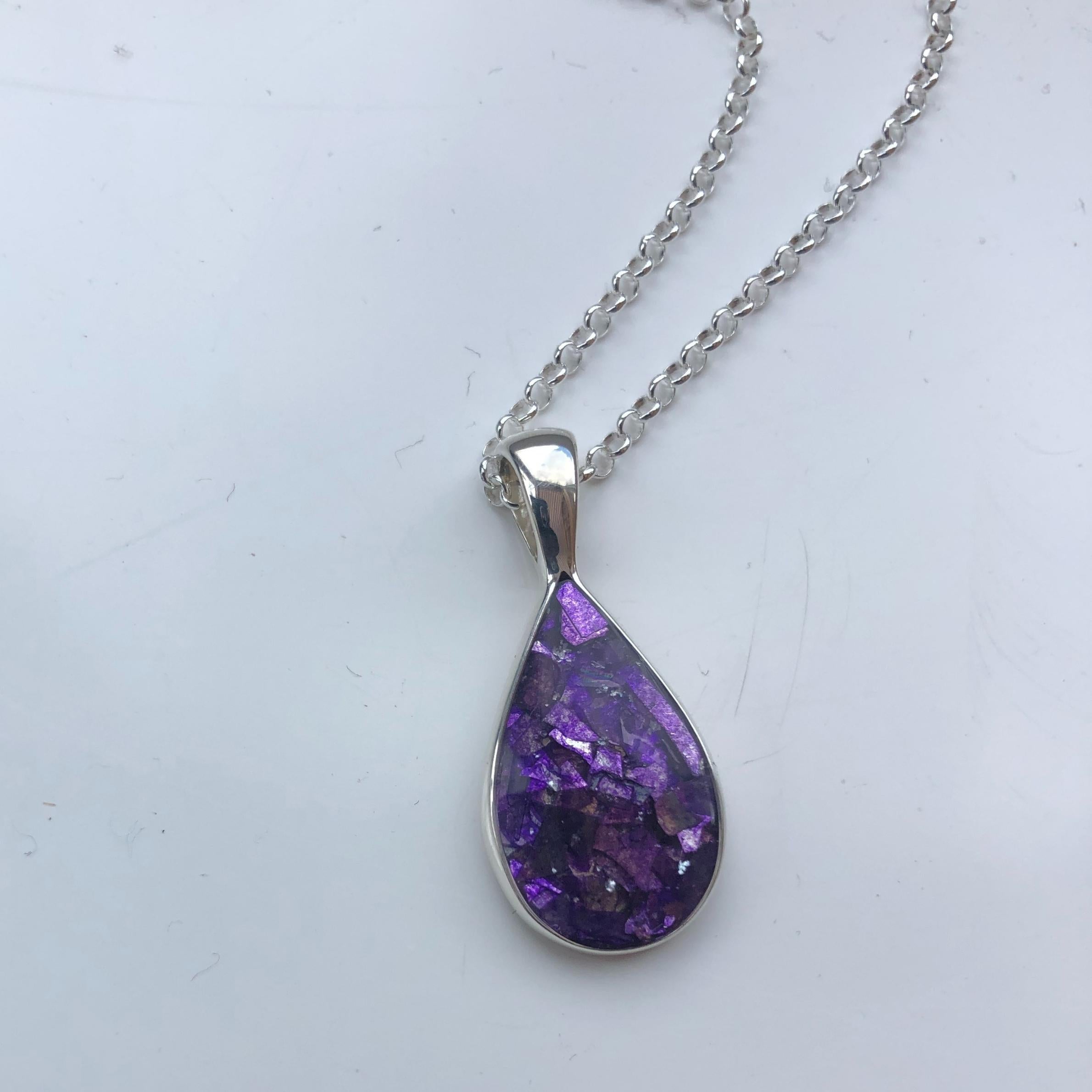 Photograph of purple ashes teardrop necklace, on silver chain. The background is light in colour.