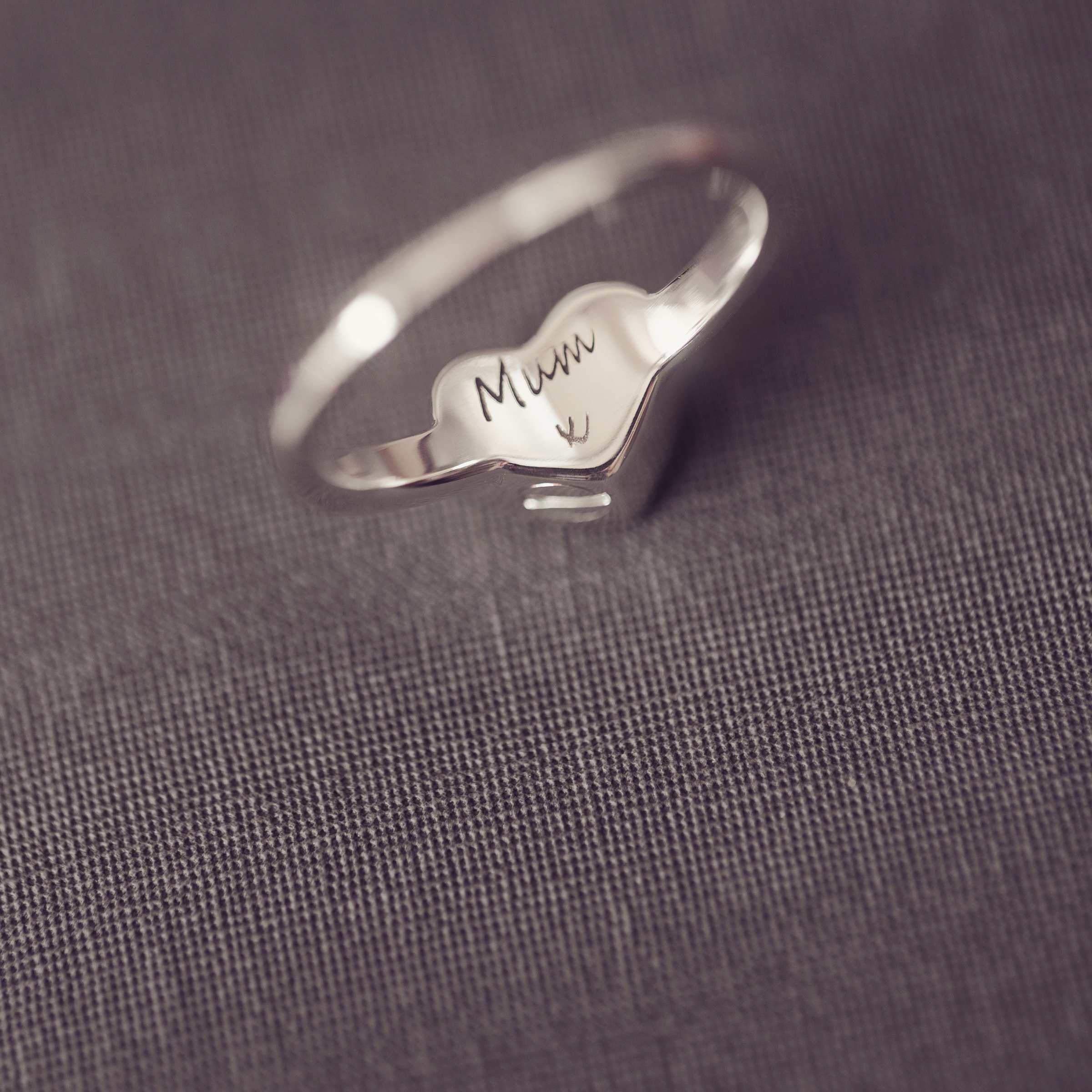 Silver ring with 'Mum x' engraving on a gray fabric background
