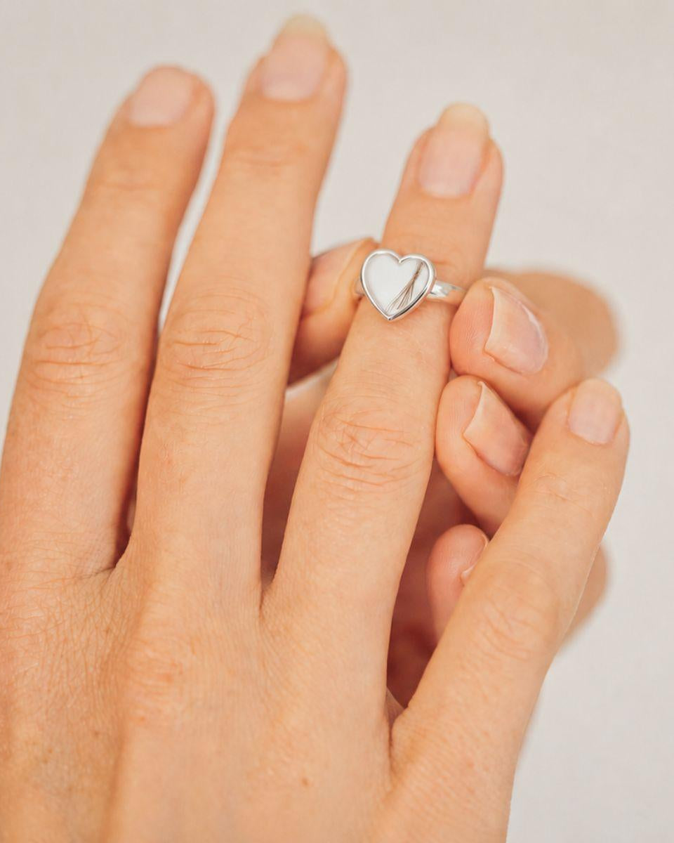 Hand wearing a silver heart-shaped ring on a plain background