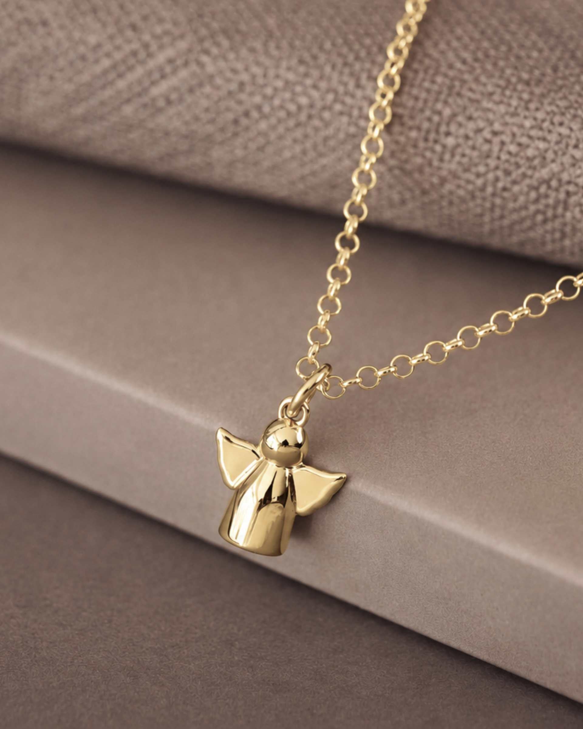 Gold pendant with chain in the shape of an angel on a brown backgound.