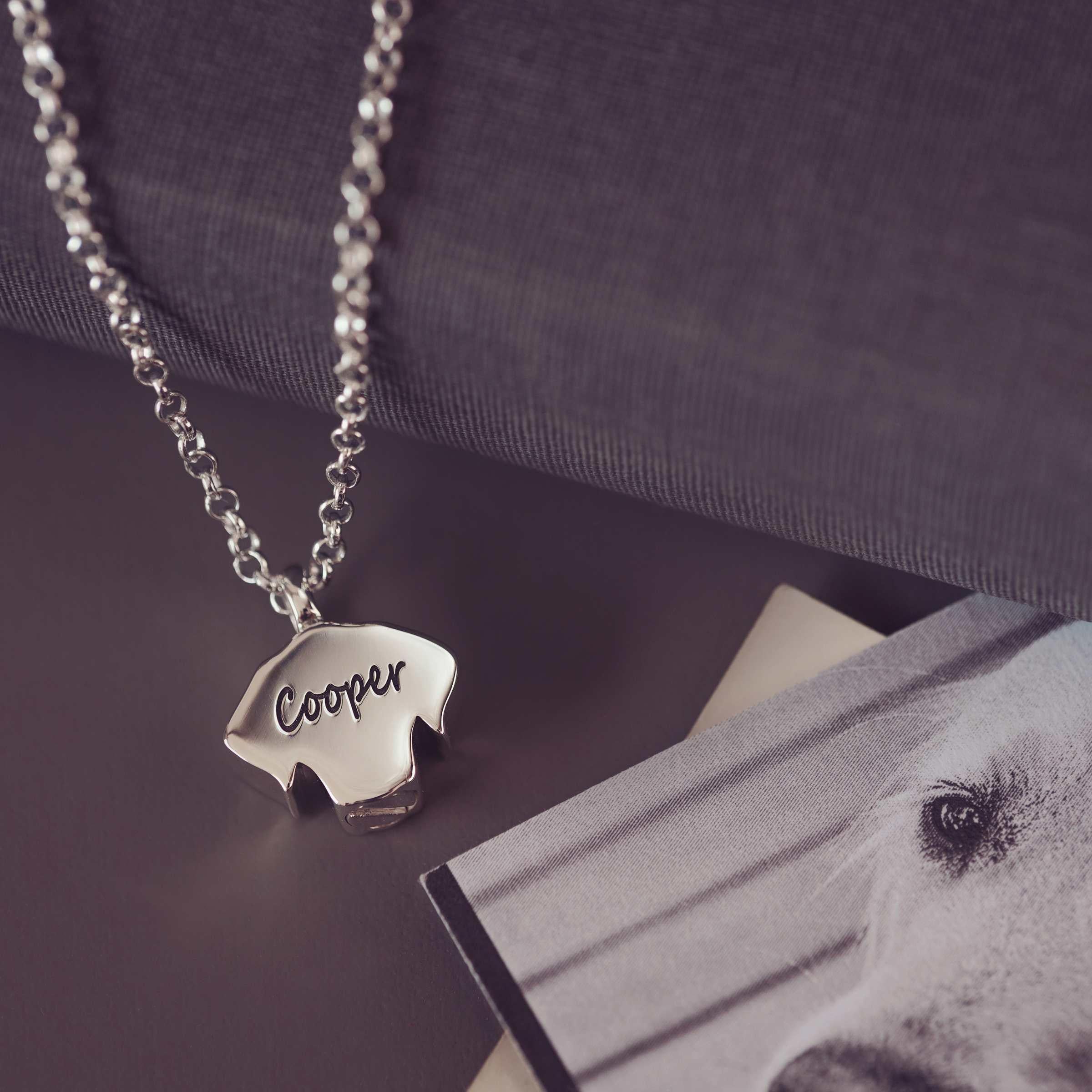 Silver necklace with a dog-shaped pendant displaying 'Cooper' on a dark surface with a photo of a dog.