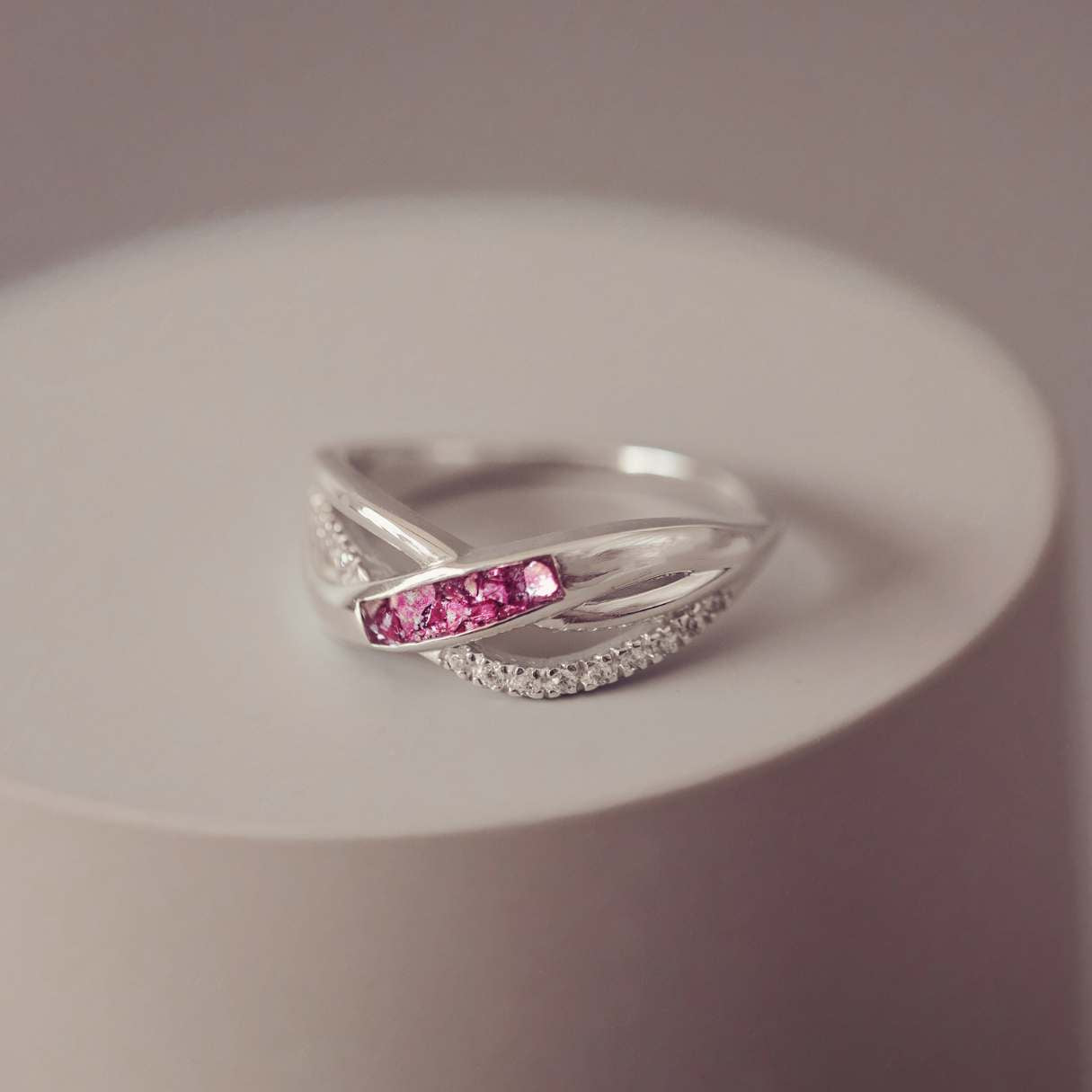 Silver ring with pink cremation ashes on a white surface