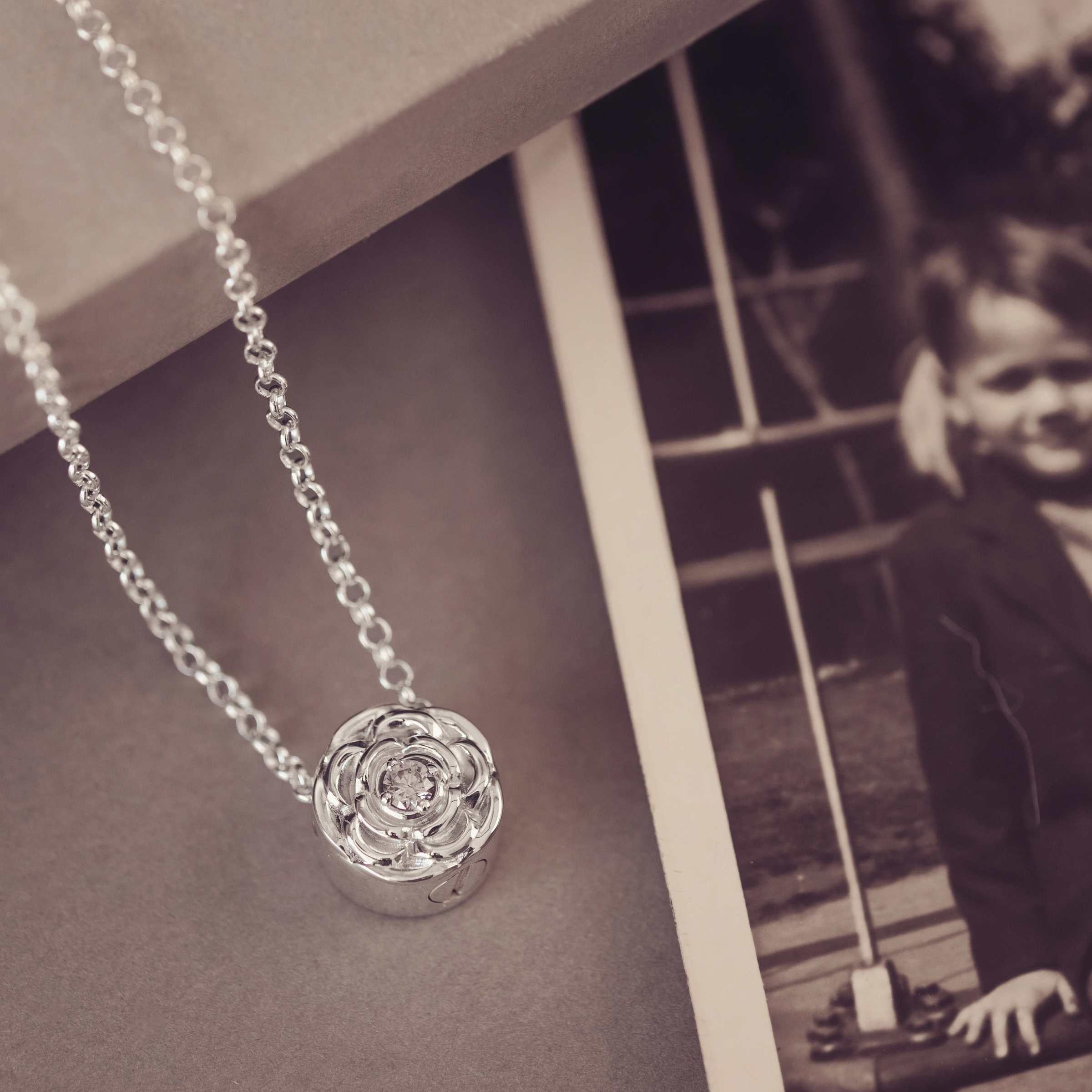Silver necklace with a floral pendant on a textured surface next to a black and white photo of a child.