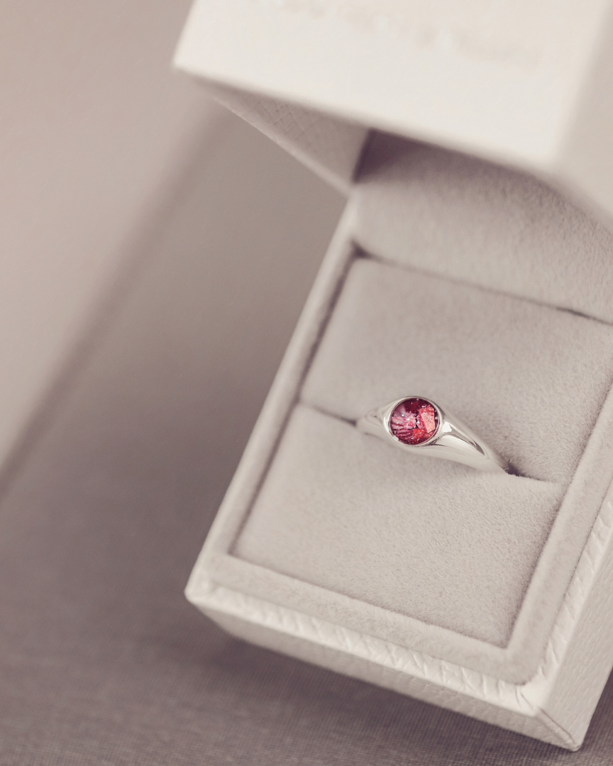 Silver ring with a red gemstone in an open jewelry box on a neutral background
