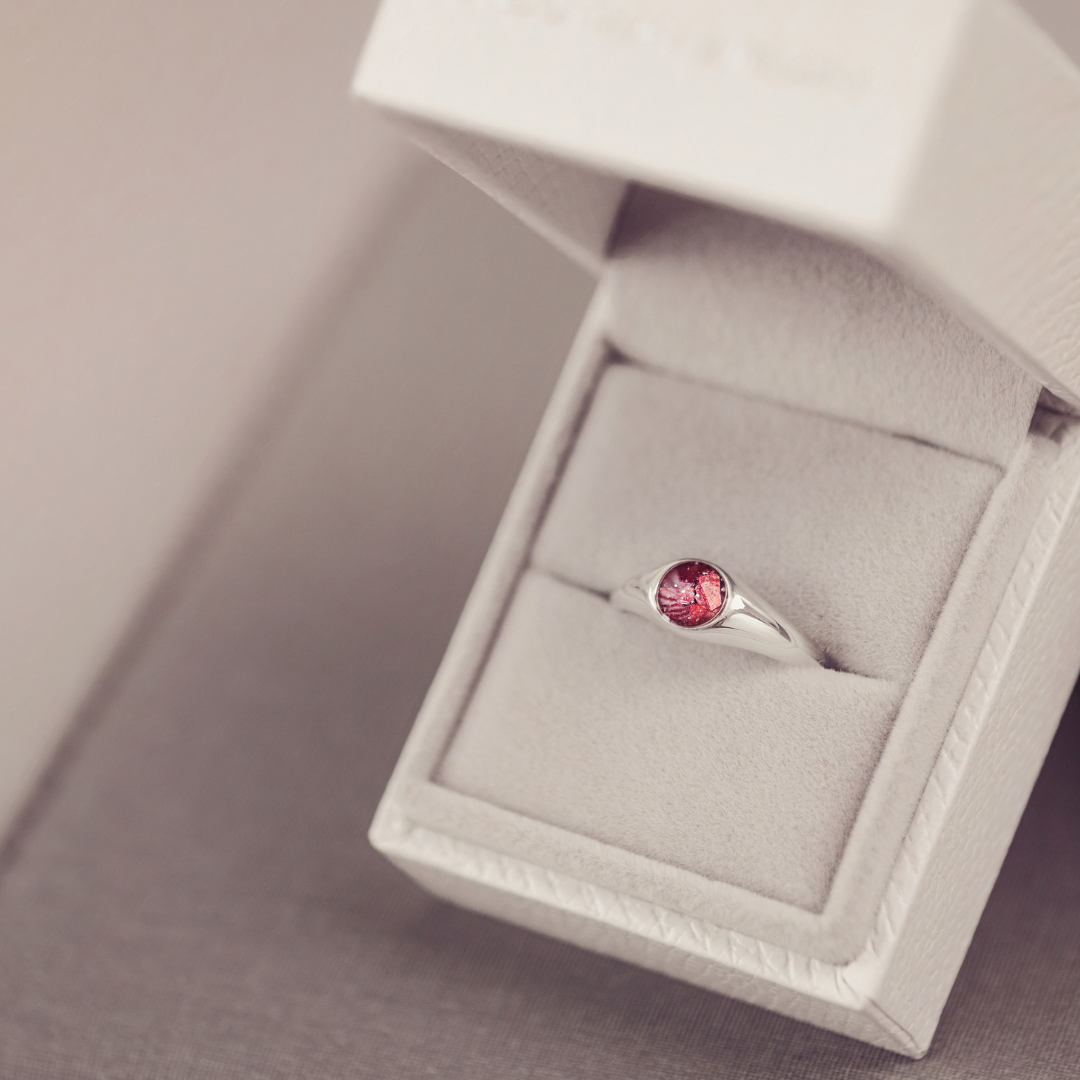 Silver ring with a red gemstone in an open jewelry box on a neutral background