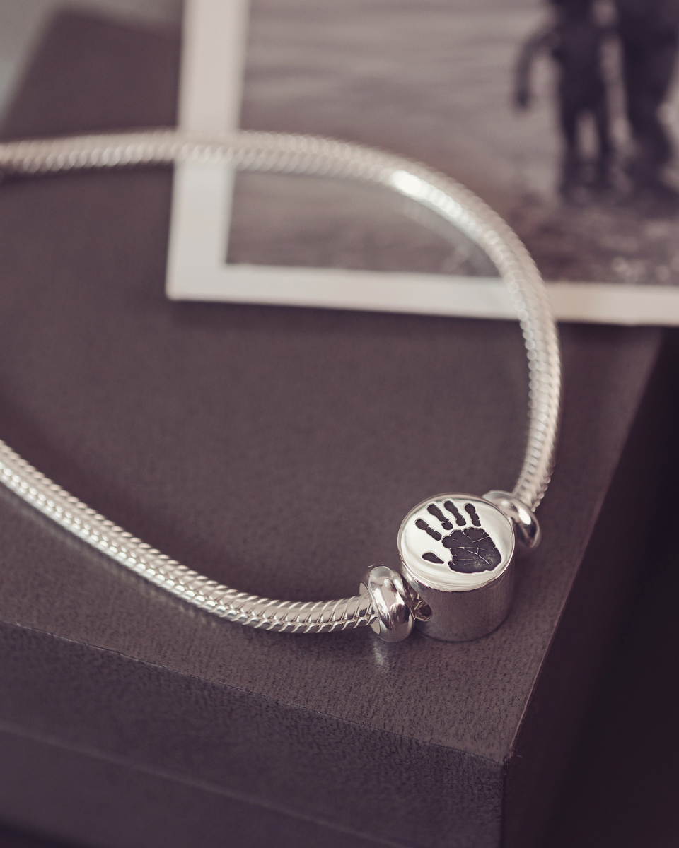 Silver bracelet with a handprint charm on a dark surface
