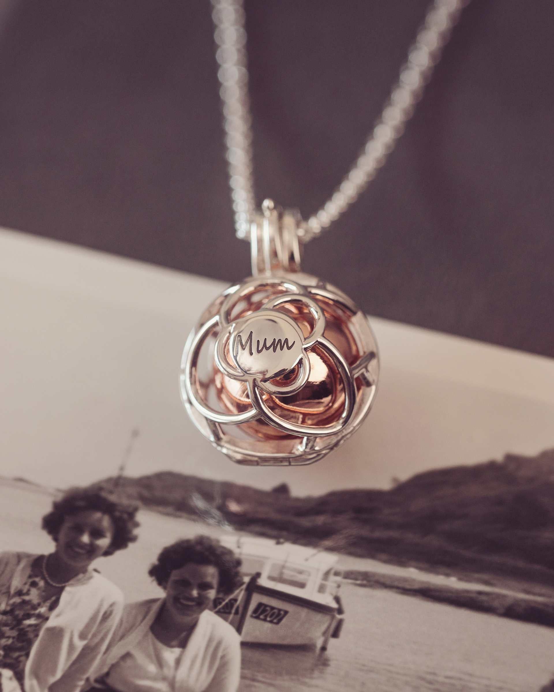 Silver and Rose gold pendant with 'Mum' engraving on a chain, over an old photograph of two women by a boat.