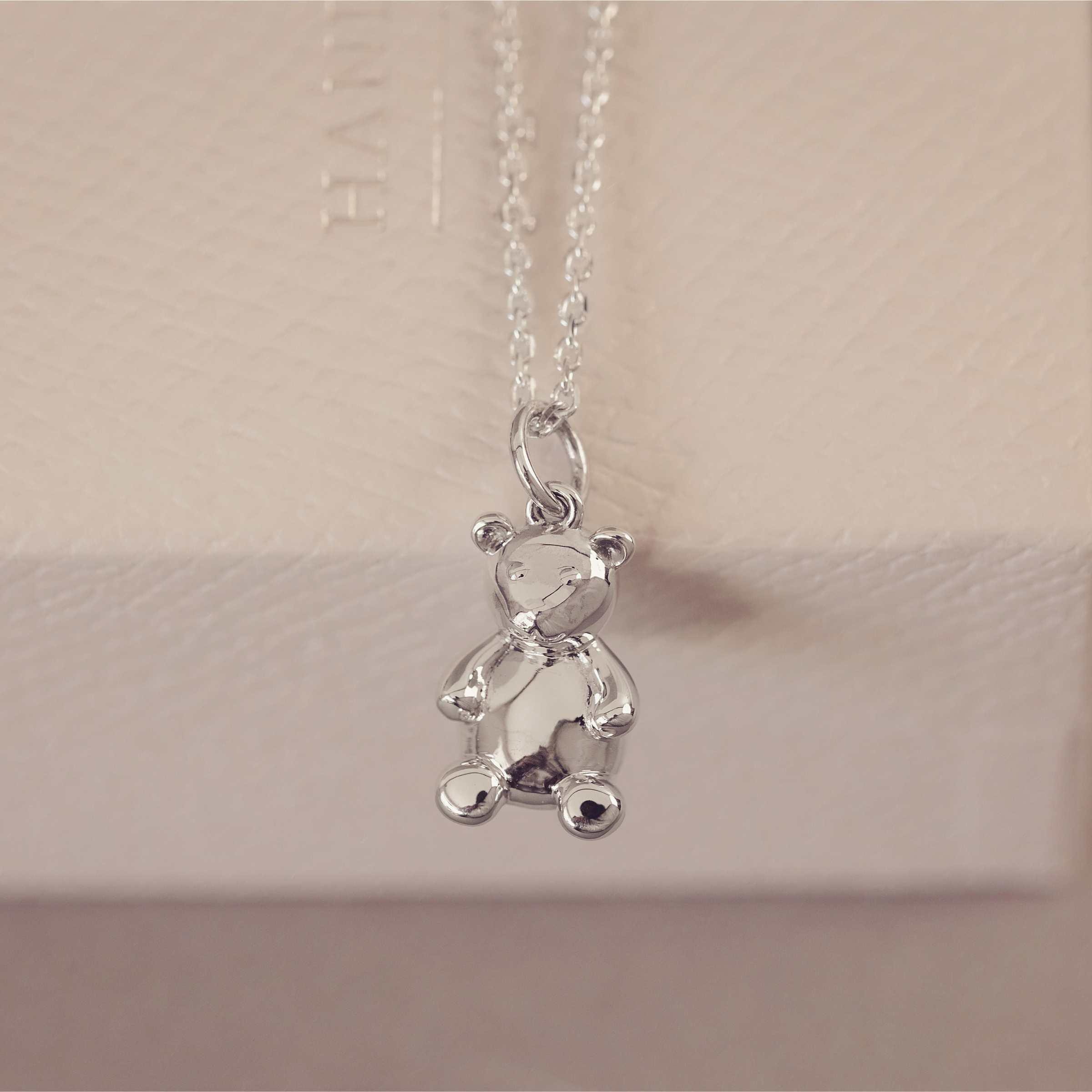 Silver teddy bear pendant on a chain against a neutral background