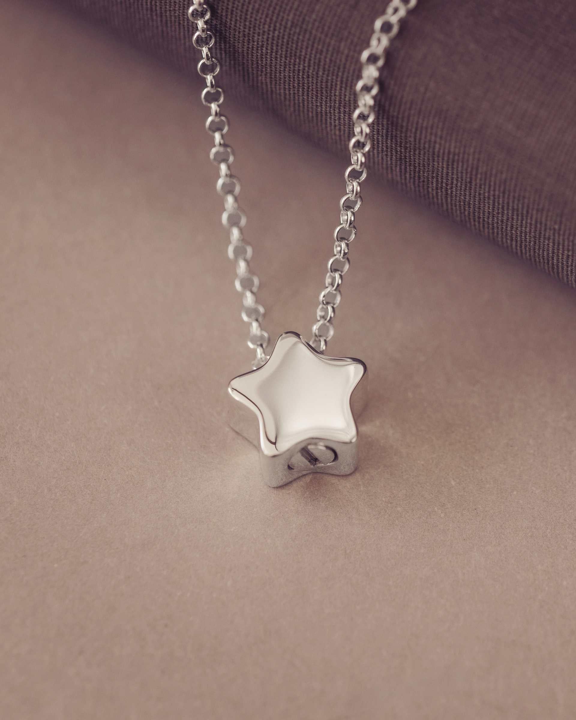 Silver star-shaped pendant on a chain against a brown background