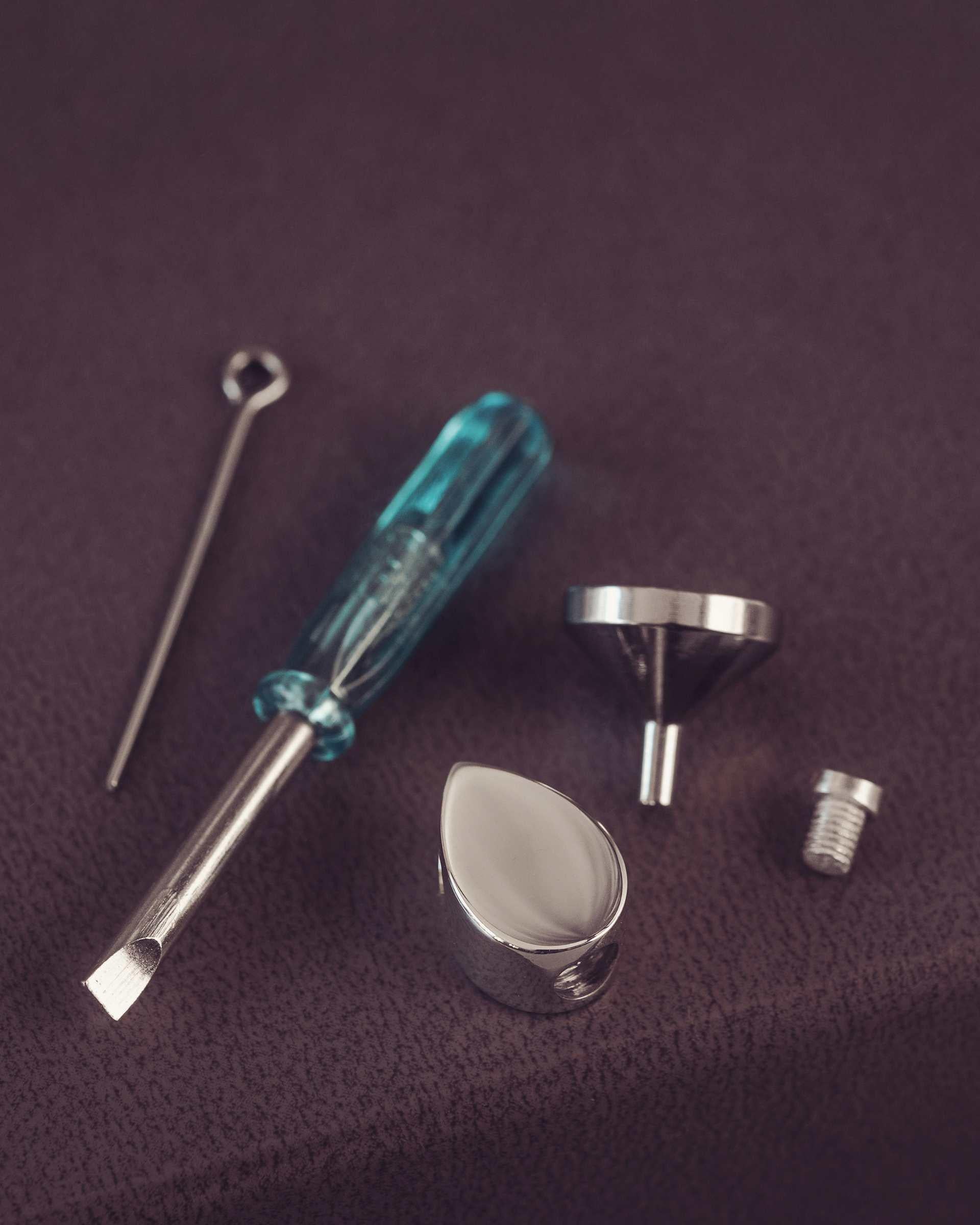 Set of small tools including a screwdriver, funnel, and other metallic items on a purple fabric background