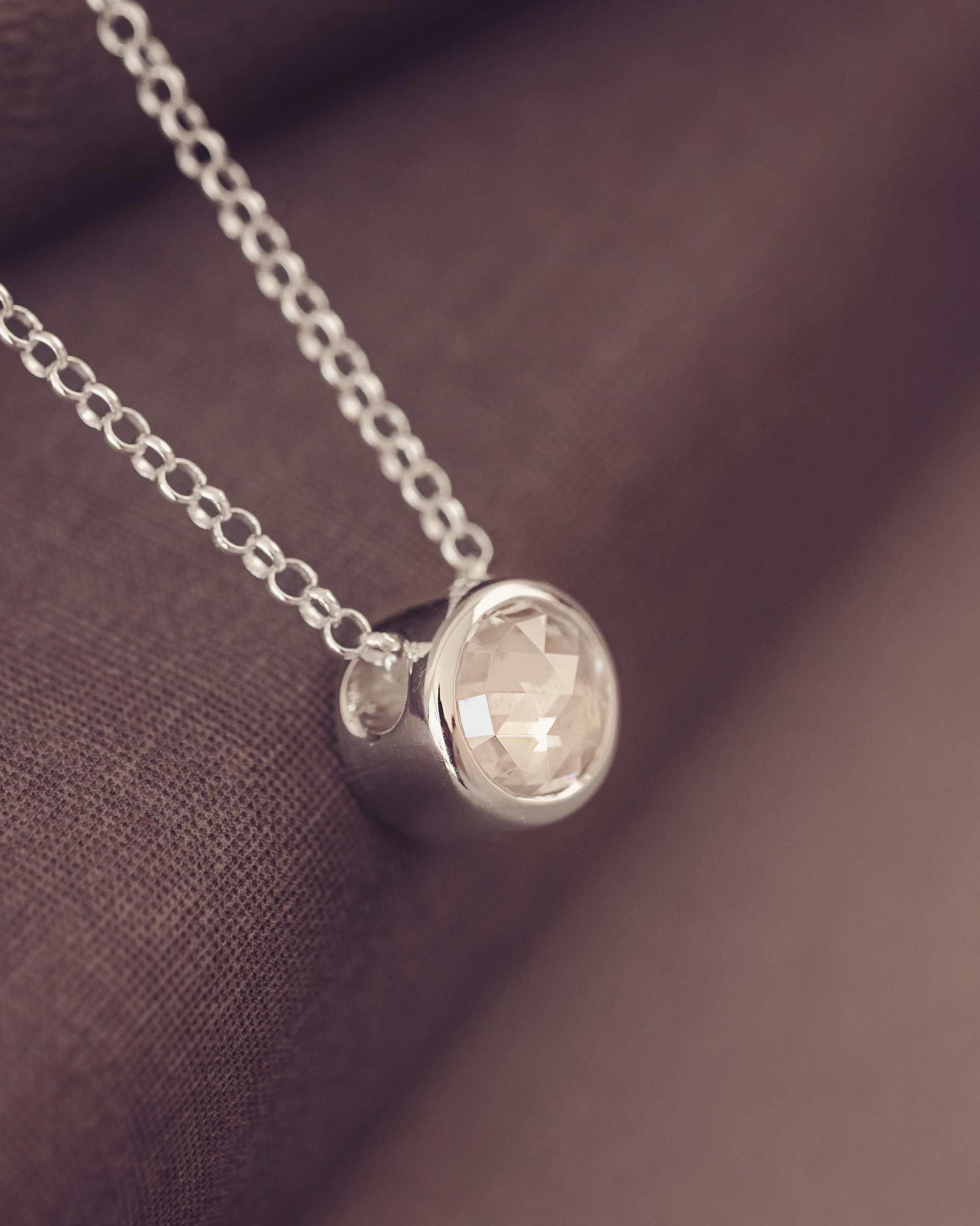 Silver necklace with a round gemtstone pendant on a brown fabric background