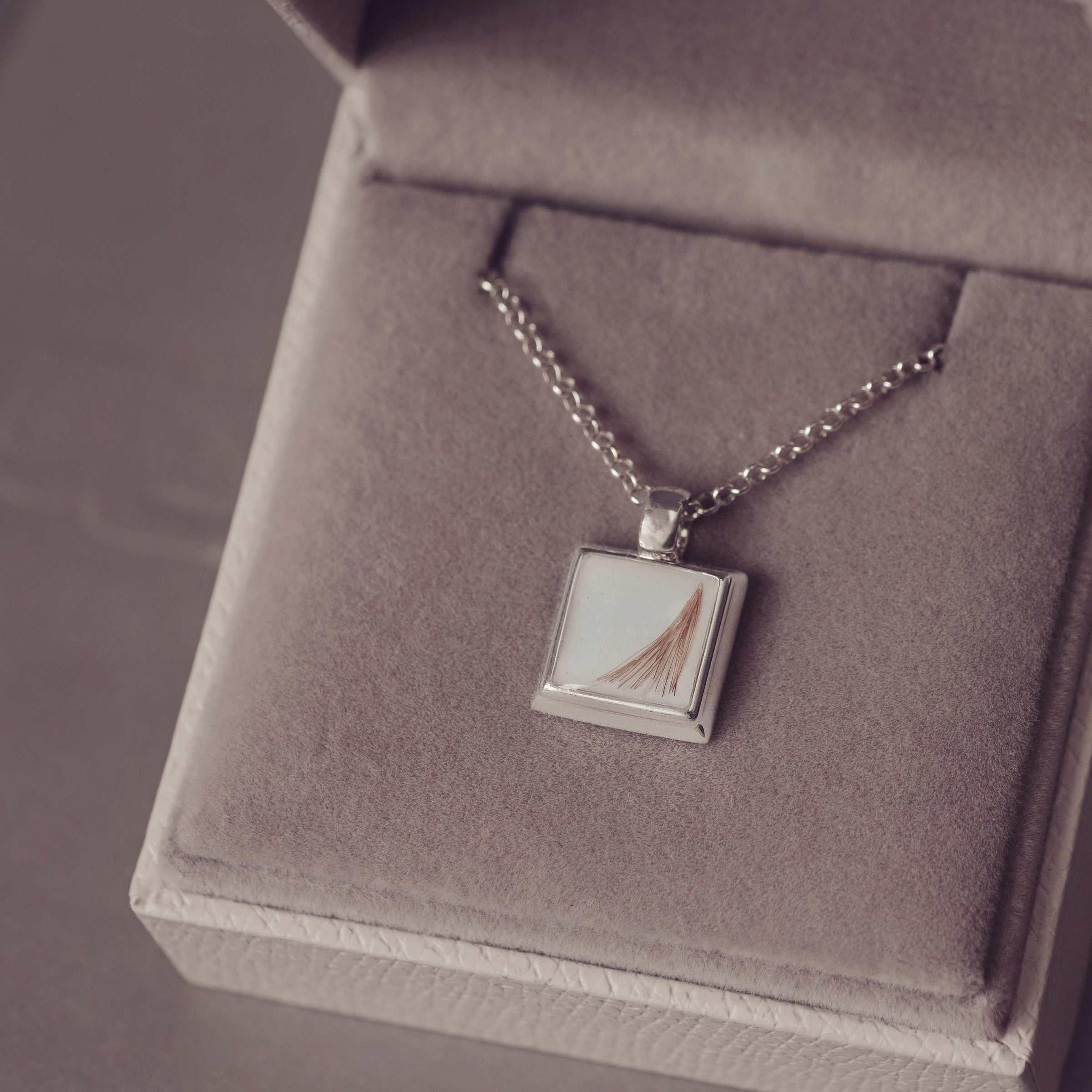 Silver necklace with a square pendant on a gray textured surface