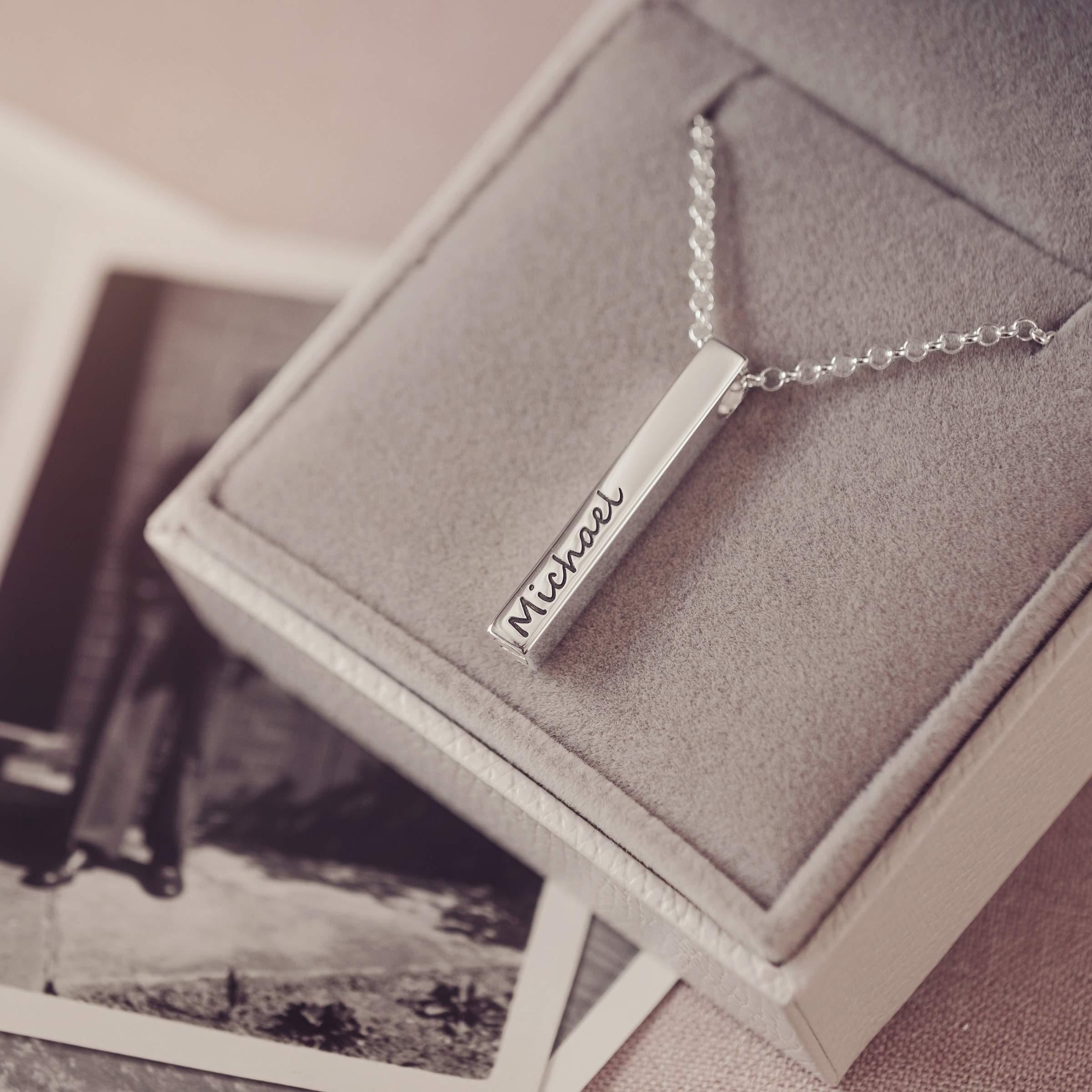 Silver necklace with 'Michael' engraving on a textured surface with blurred black and white photos in the background.
