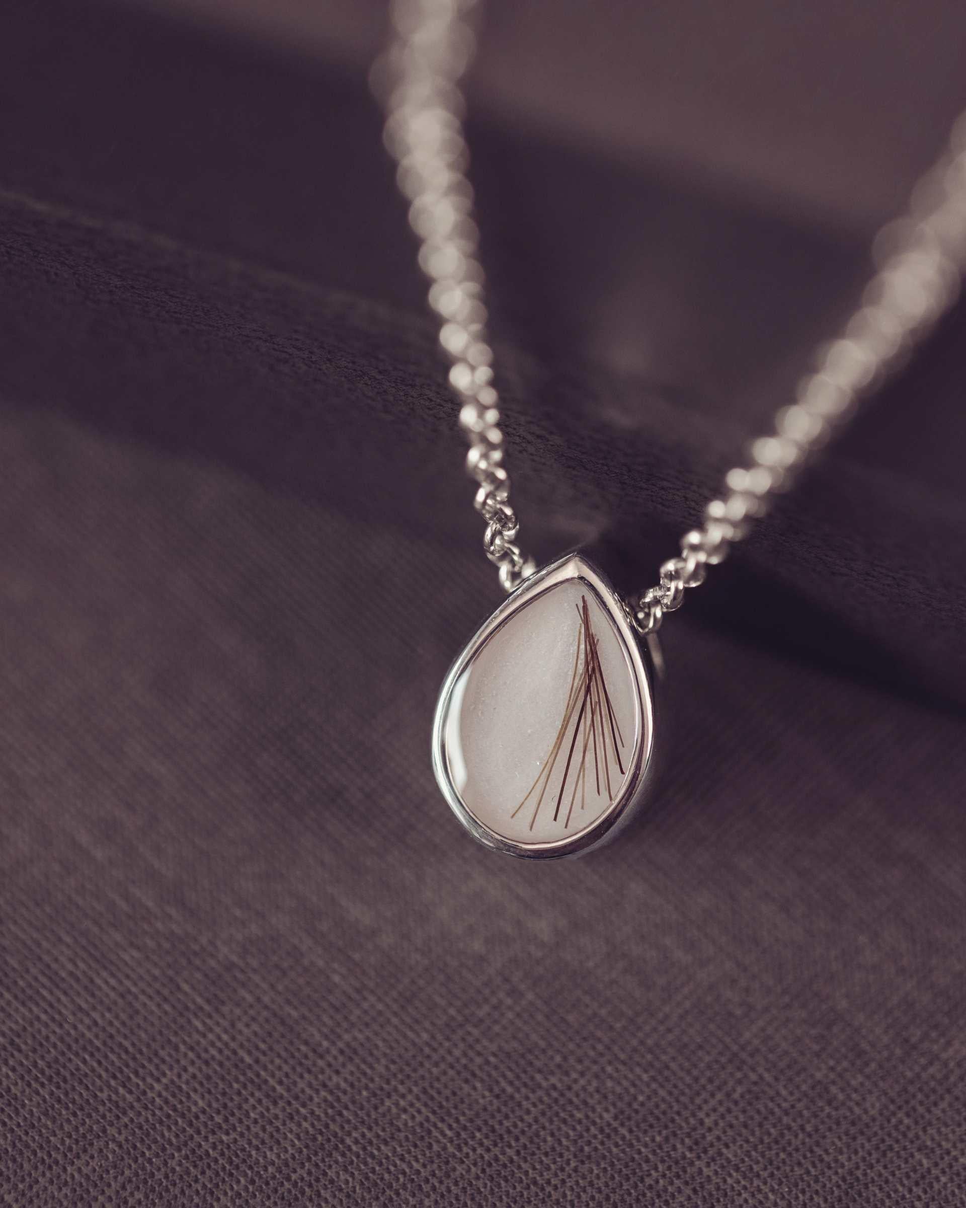 silver teardrop shaped pendant on a dark background