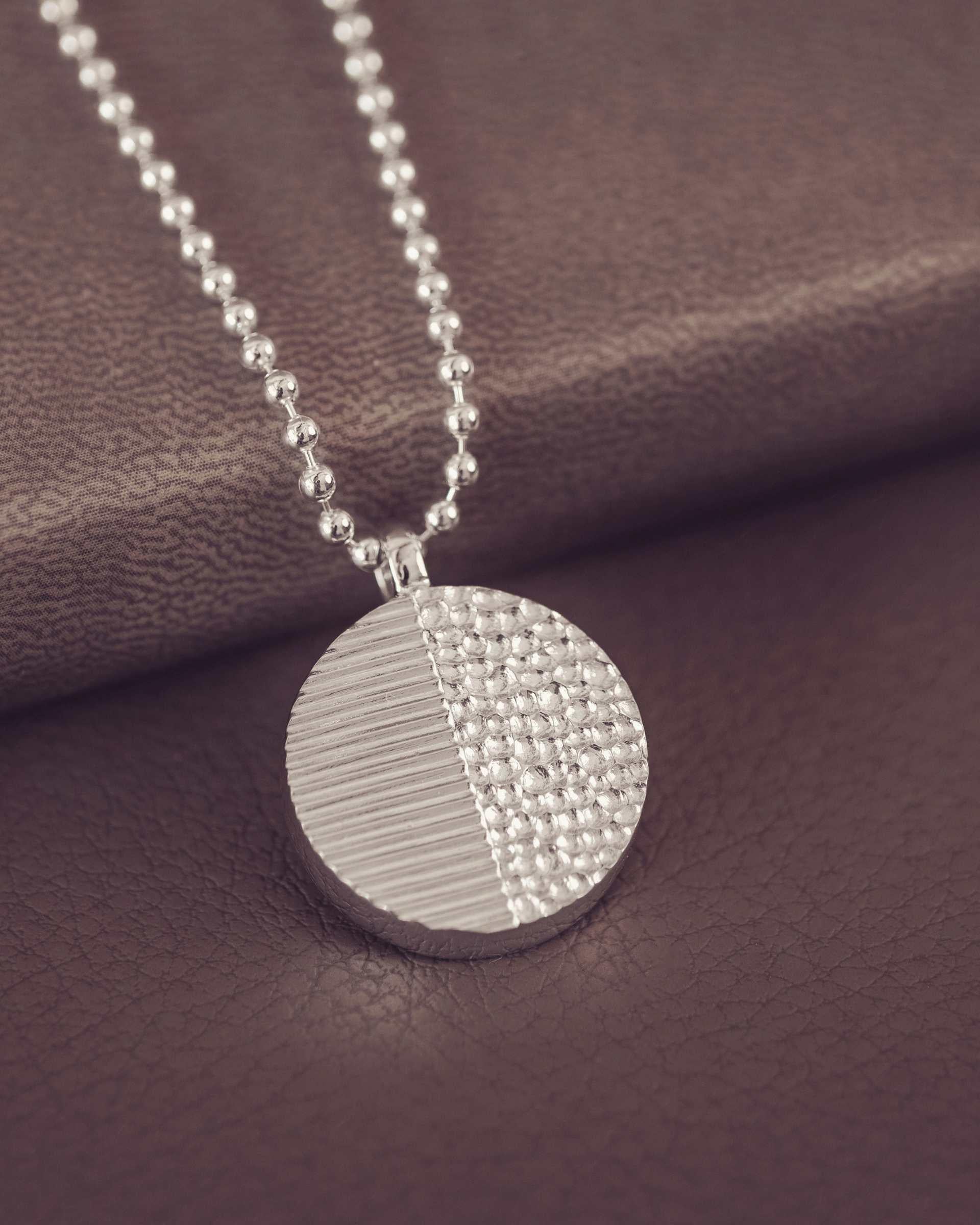 Silver necklace with a textured pendant on a brown fabric background