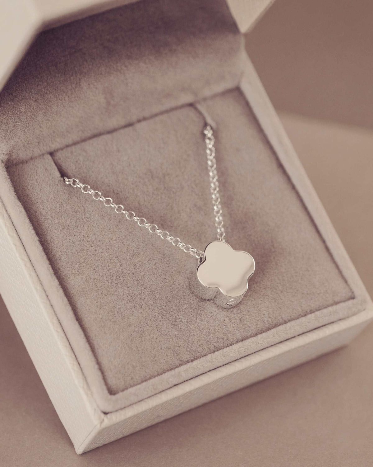 Silver necklace with a clover-shaped pendant in an open jewelry box.