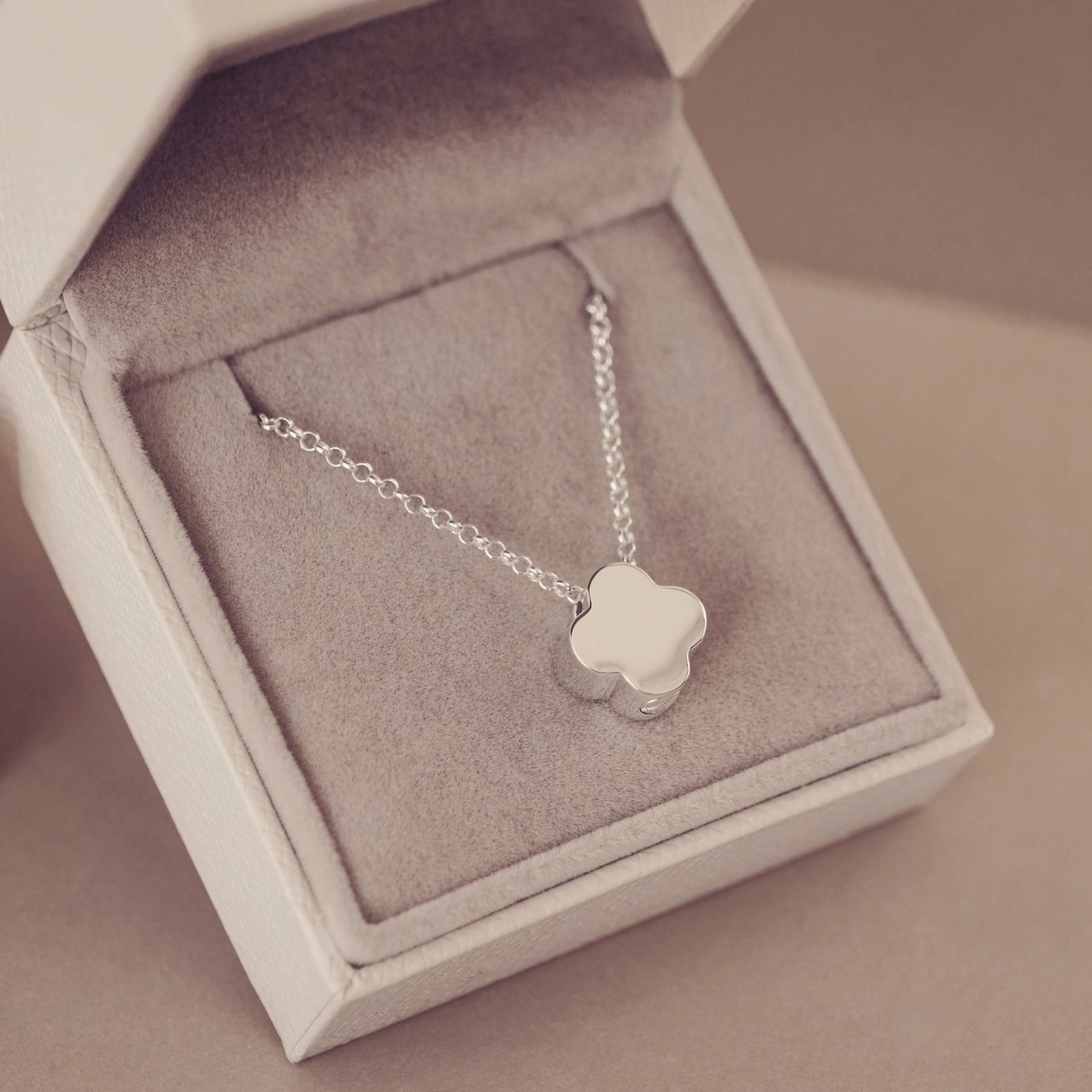 Silver necklace with a clover-shaped pendant in an open jewelry box.