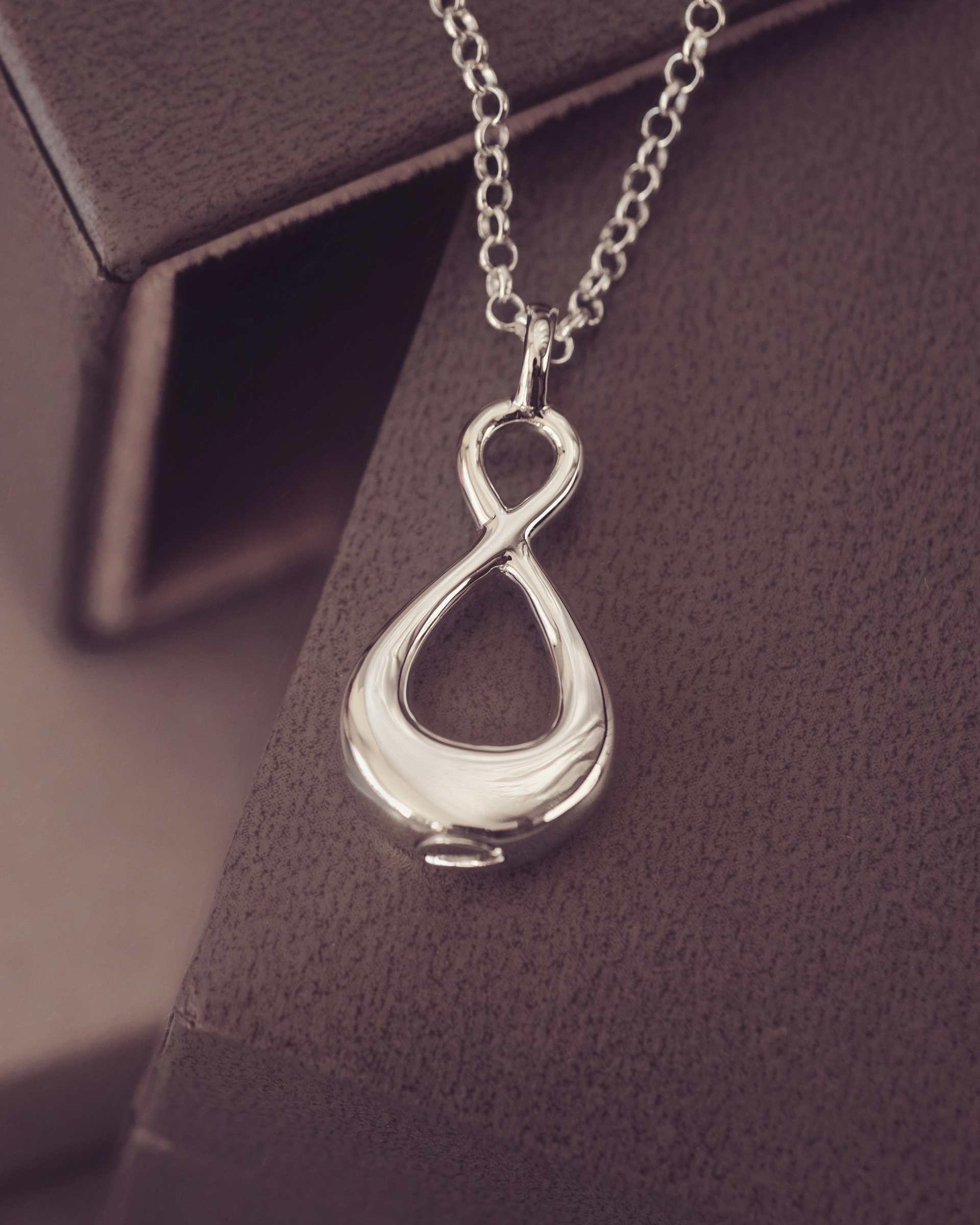 Silver infinity pendant necklace on a dark textured surface