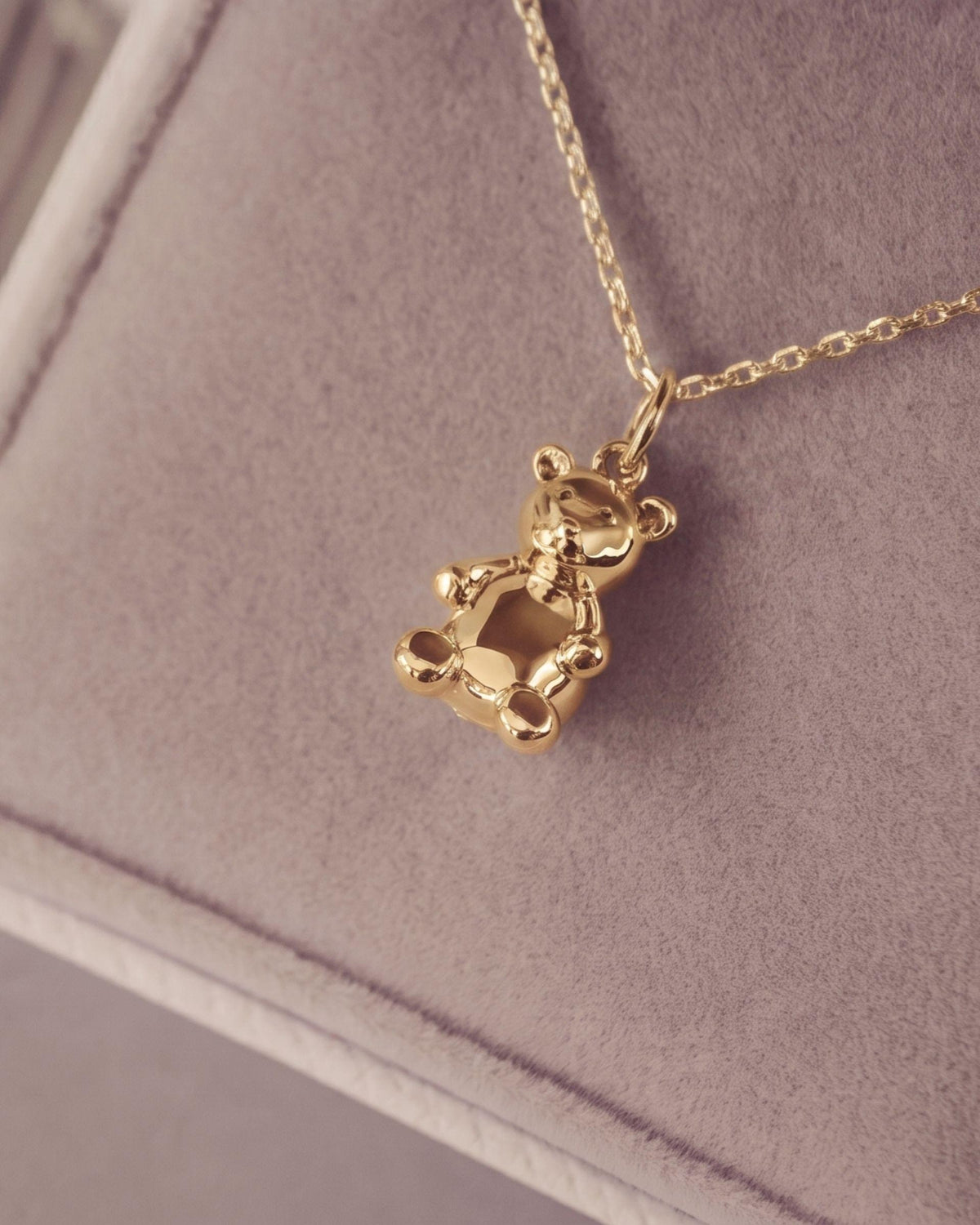 A gold teddy bear pendant necklace resting on a soft jewelry box.