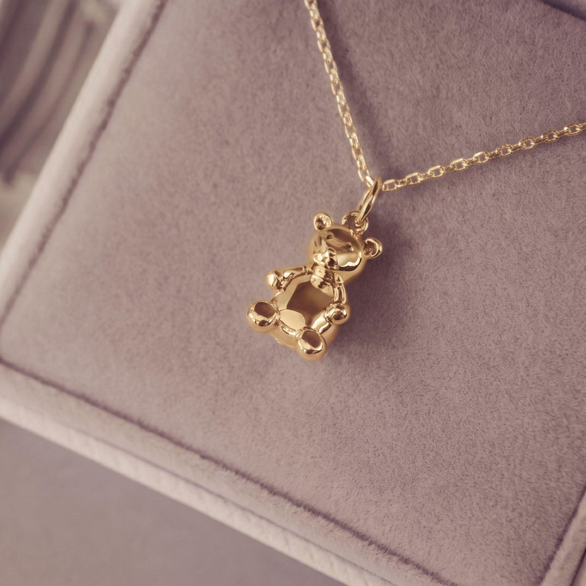 A gold teddy bear pendant necklace resting on a soft jewelry box.