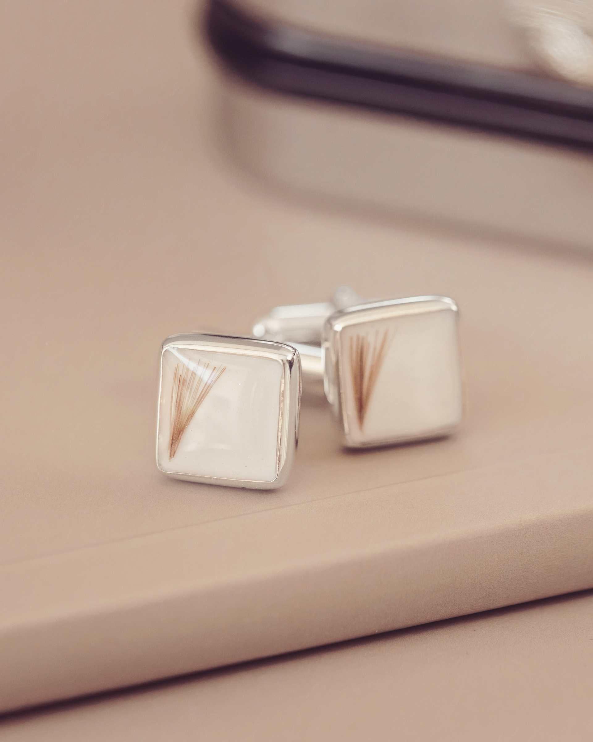 Silver square cufflinks on a beige surface