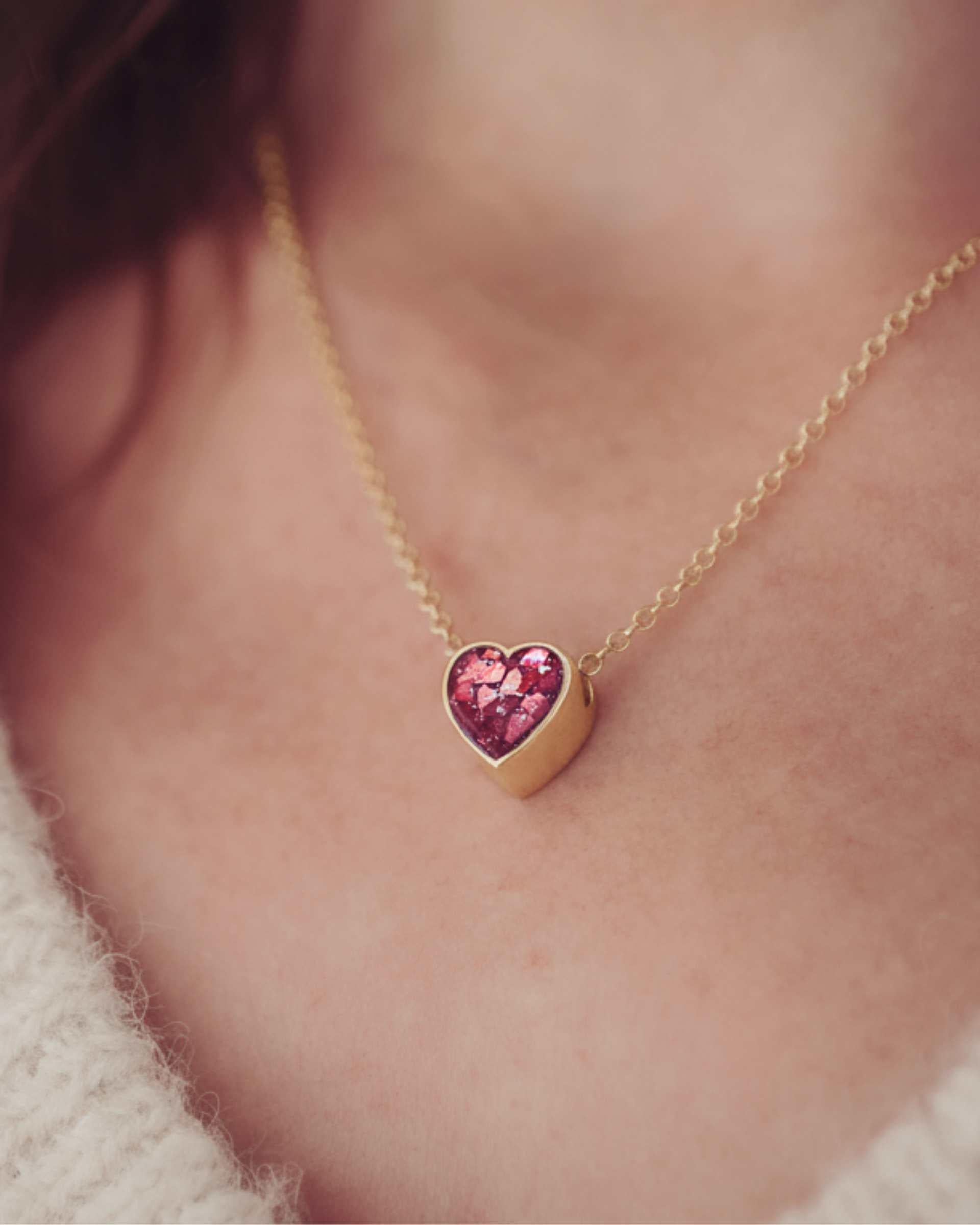 Gold necklace with a heart-shaped resin pendant worn by a person.