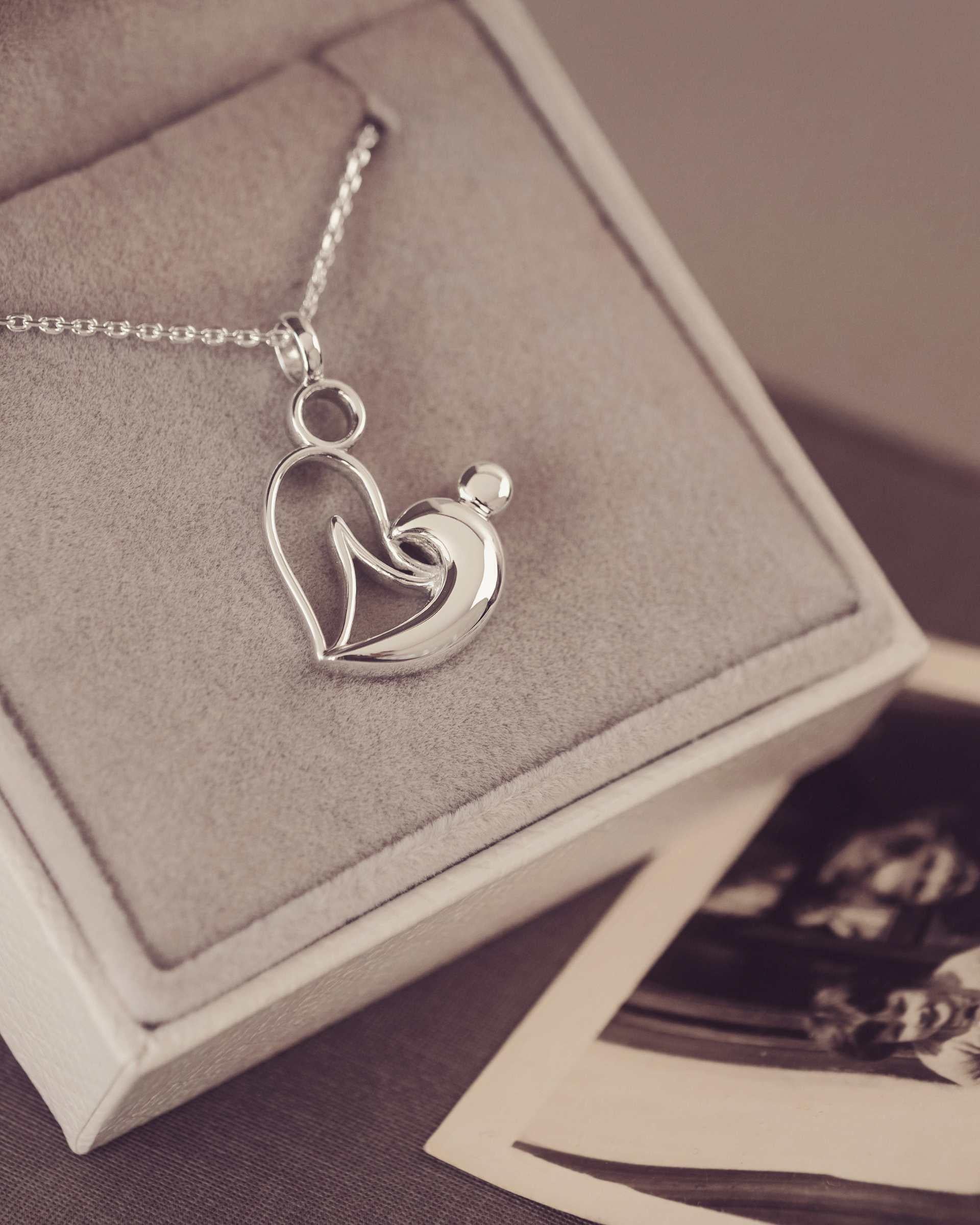 Silver necklace with two person heart pendant in a jewellery box with vintage photos.