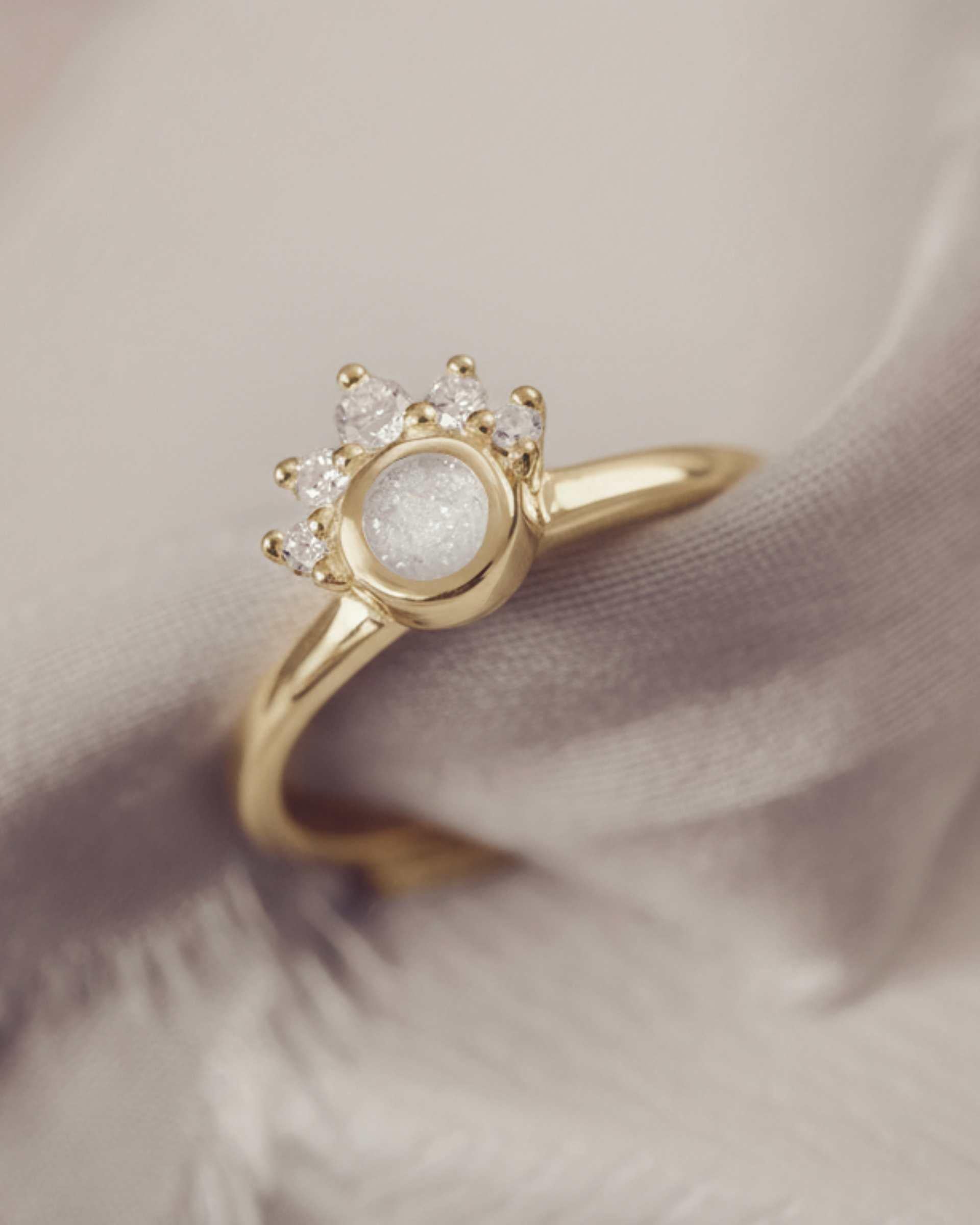 Gold cluster ring with a white sparkle resin and smaller stones on a soft fabric background