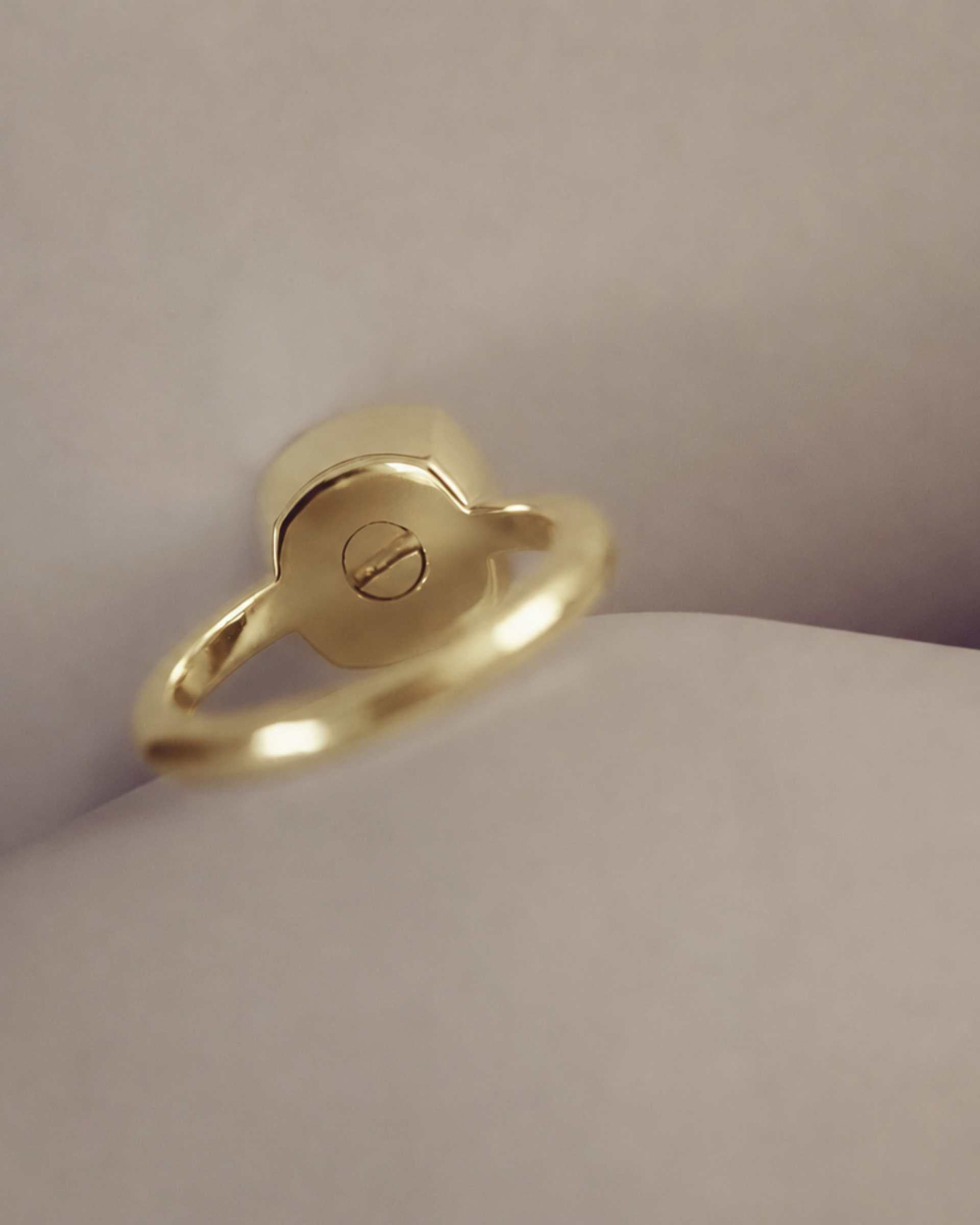 Gold ring showing a screw on a cream background