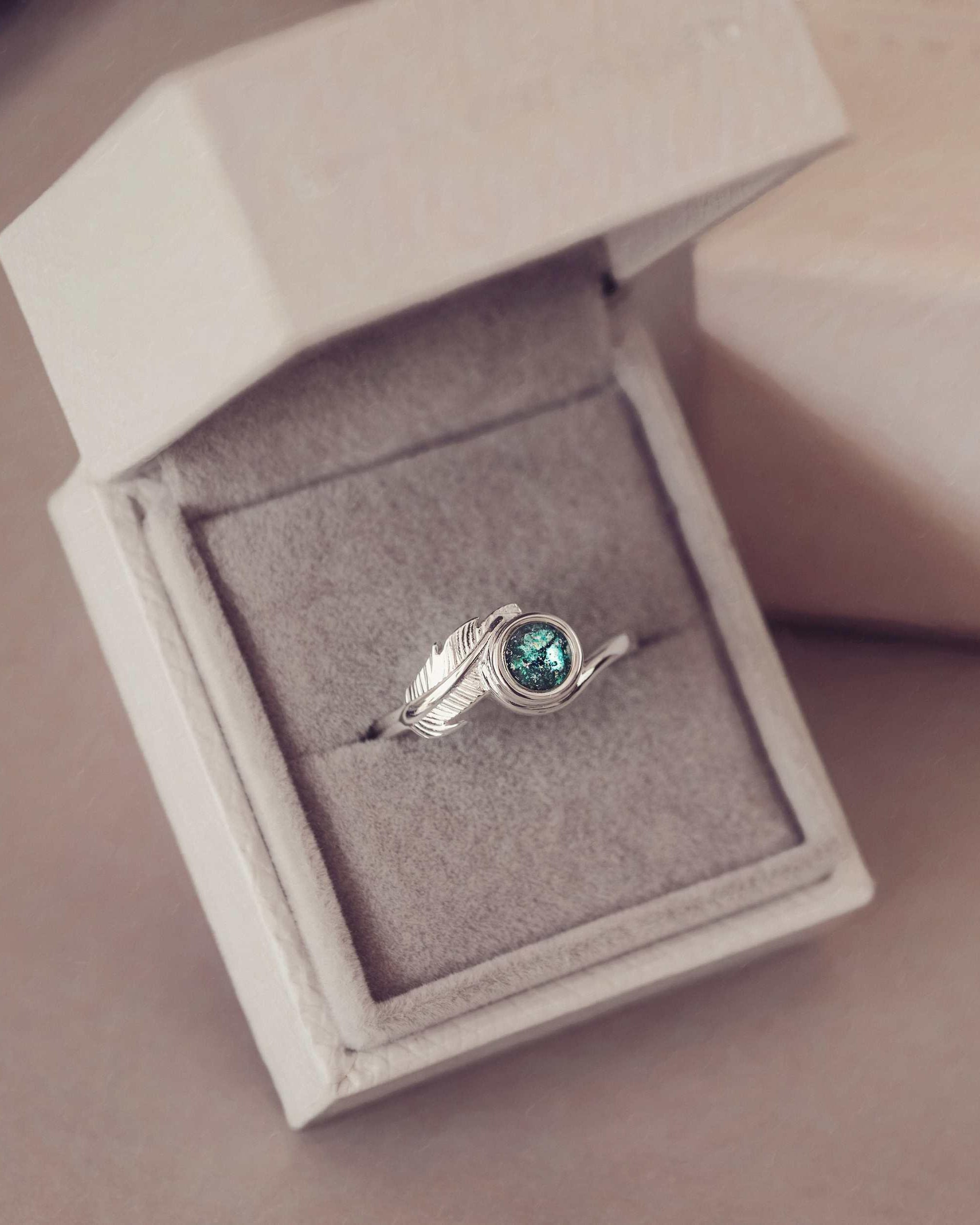 A silver ash filled feather ring in a jewellery box