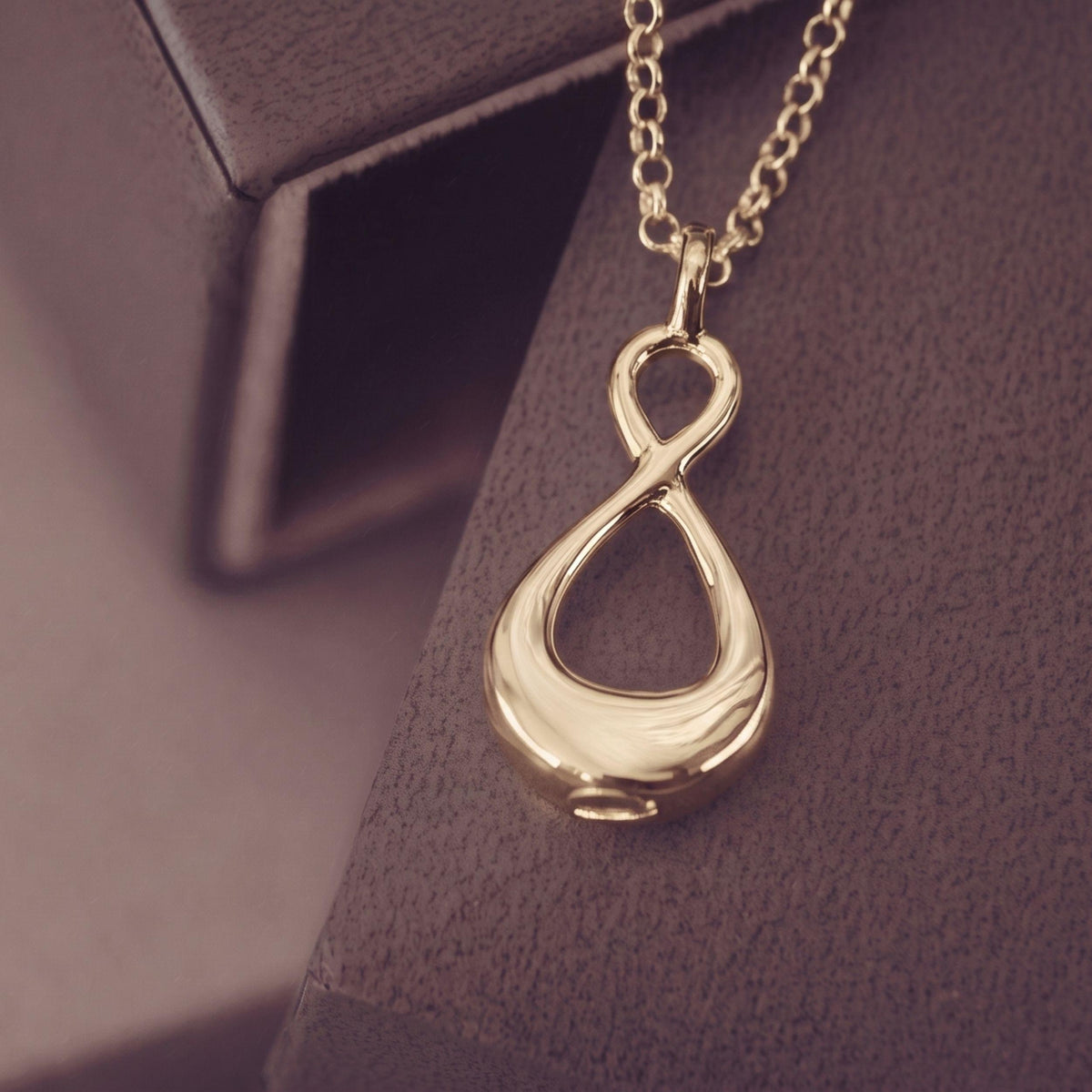A gold infinity pendant necklace resting on a a dark textured background