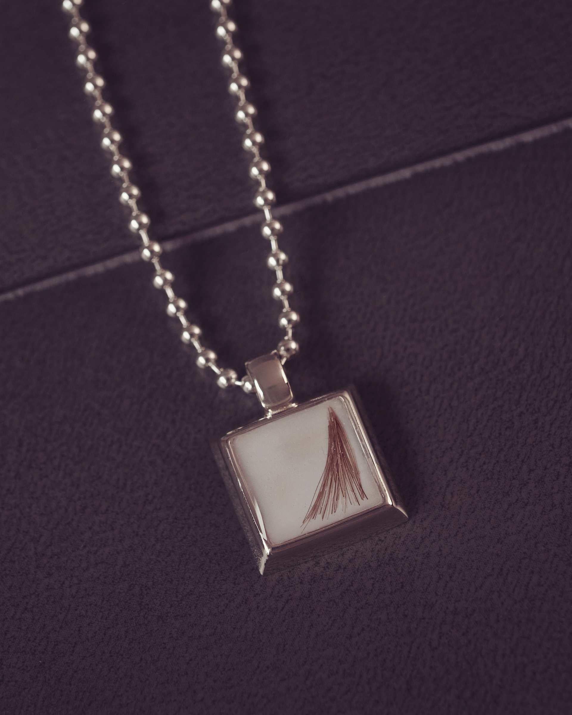 Silver necklace with a square pendant on a dark purple background