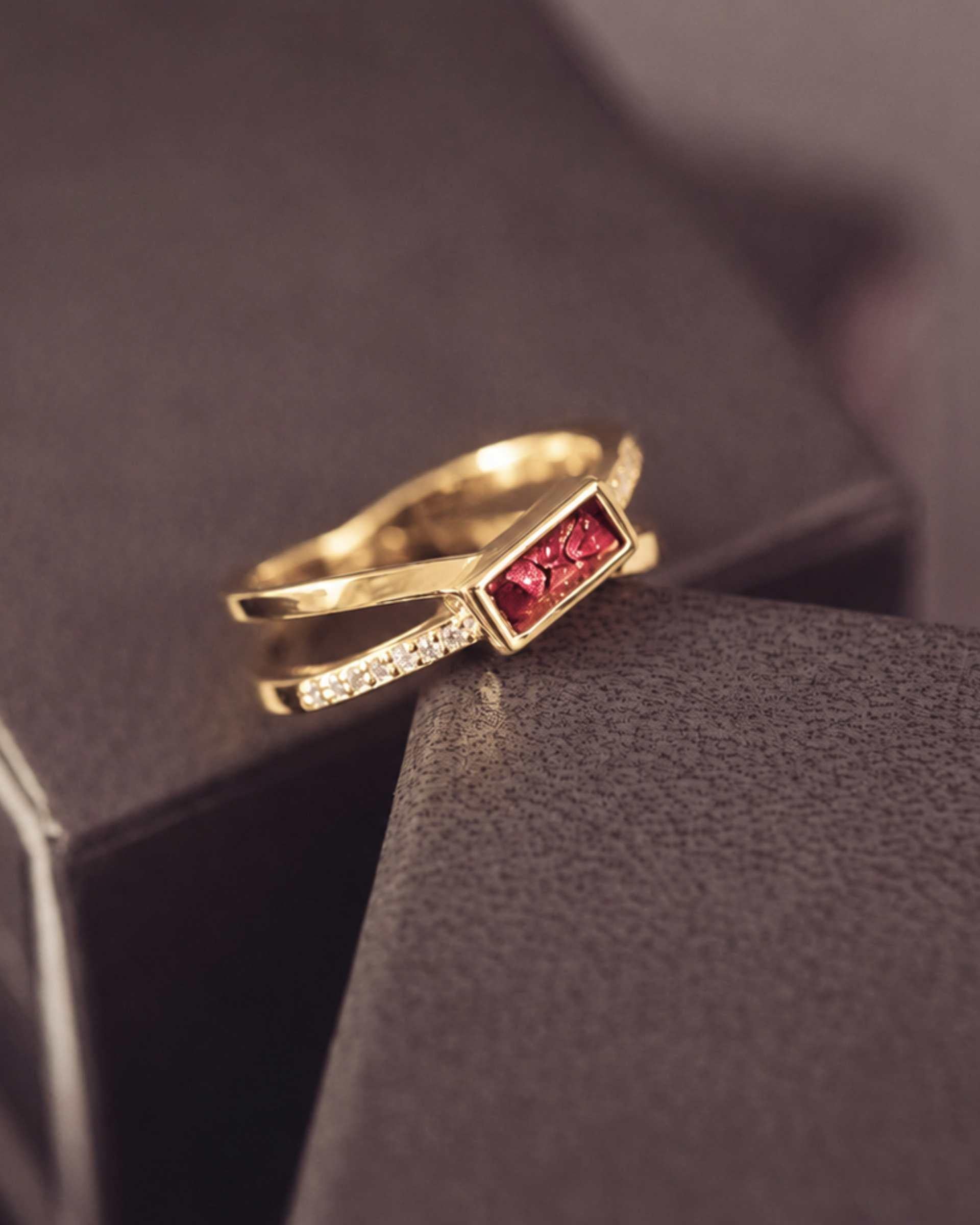 gold criss cross ring with a red rectangle ash stone and gemstones on a dark background