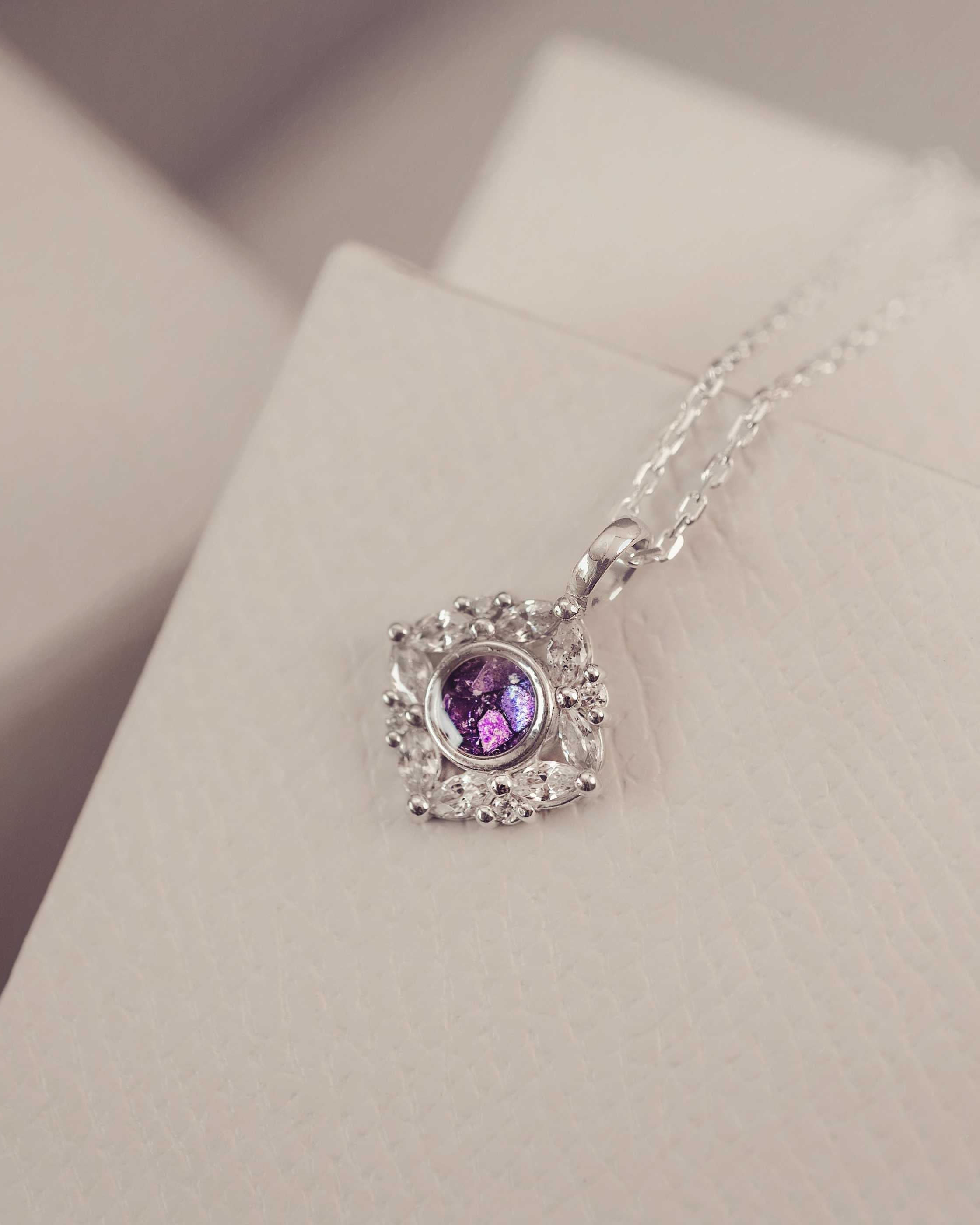 Silver necklace with a purple gemstone pendant on a light pink surface