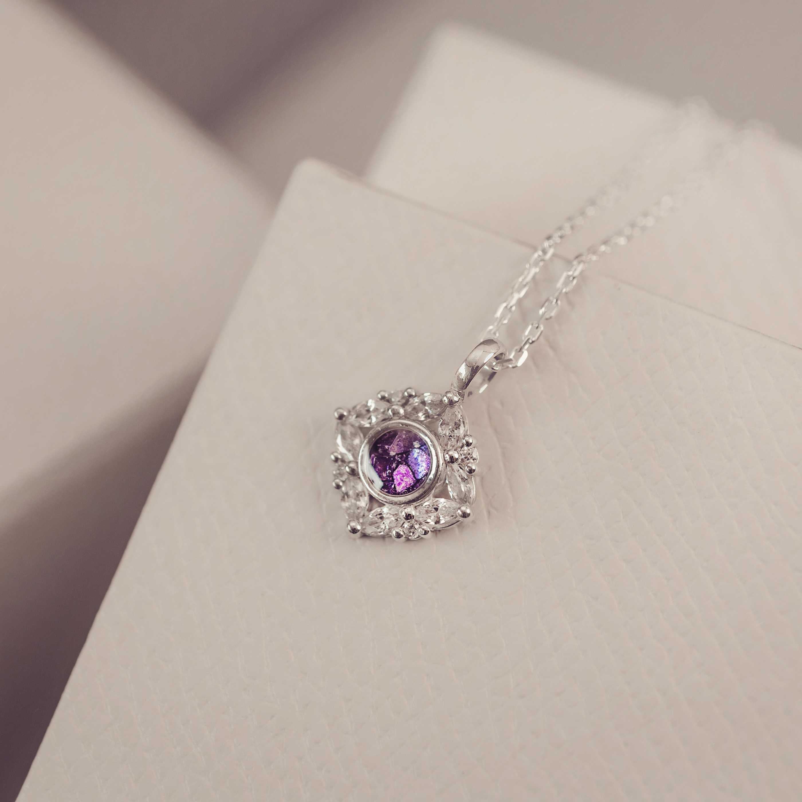 Silver necklace with a purple gemstone pendant on a light pink surface
