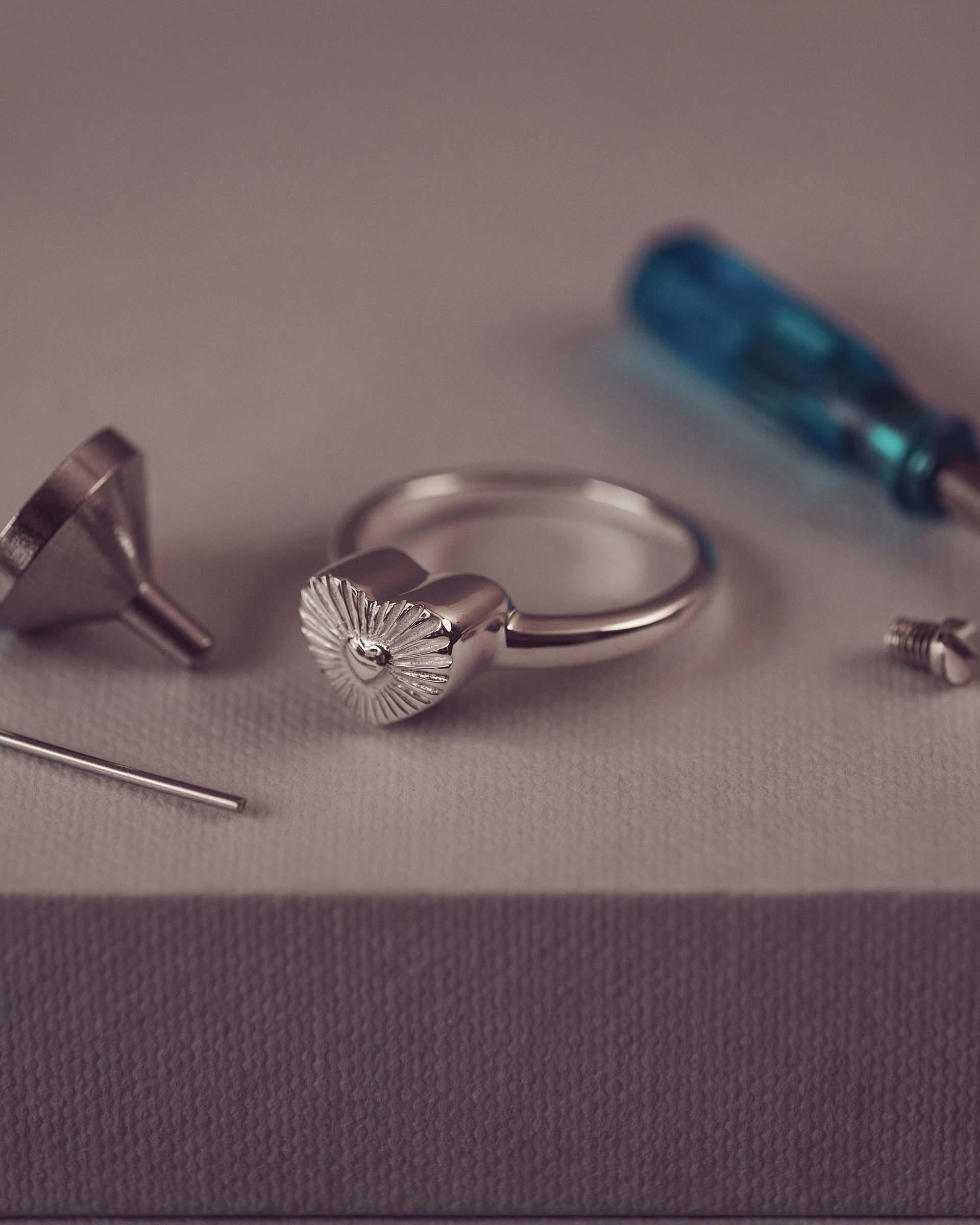 Silver ring with heart design on a gray surface with tools.