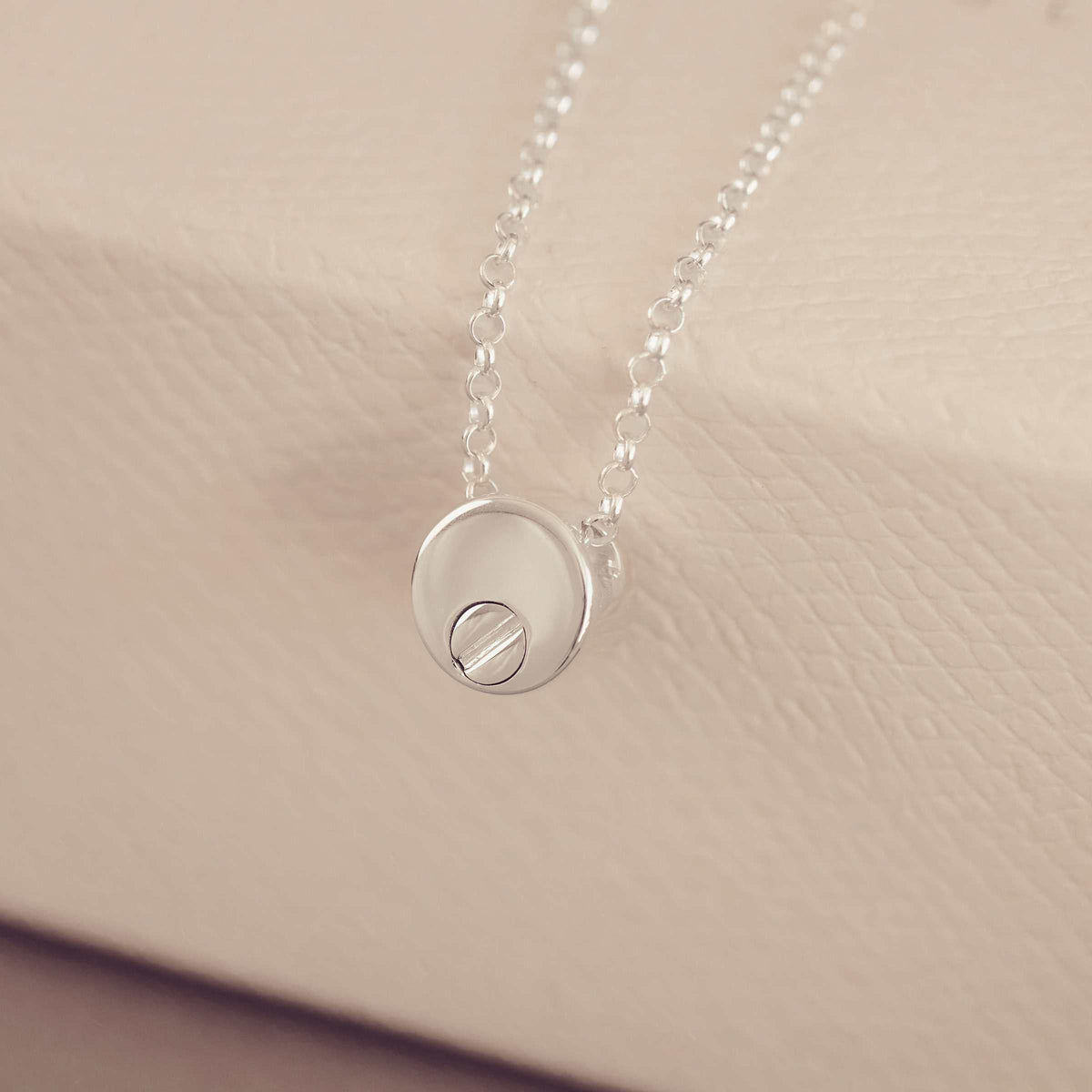 Silver necklace with a round pendant on a beige background