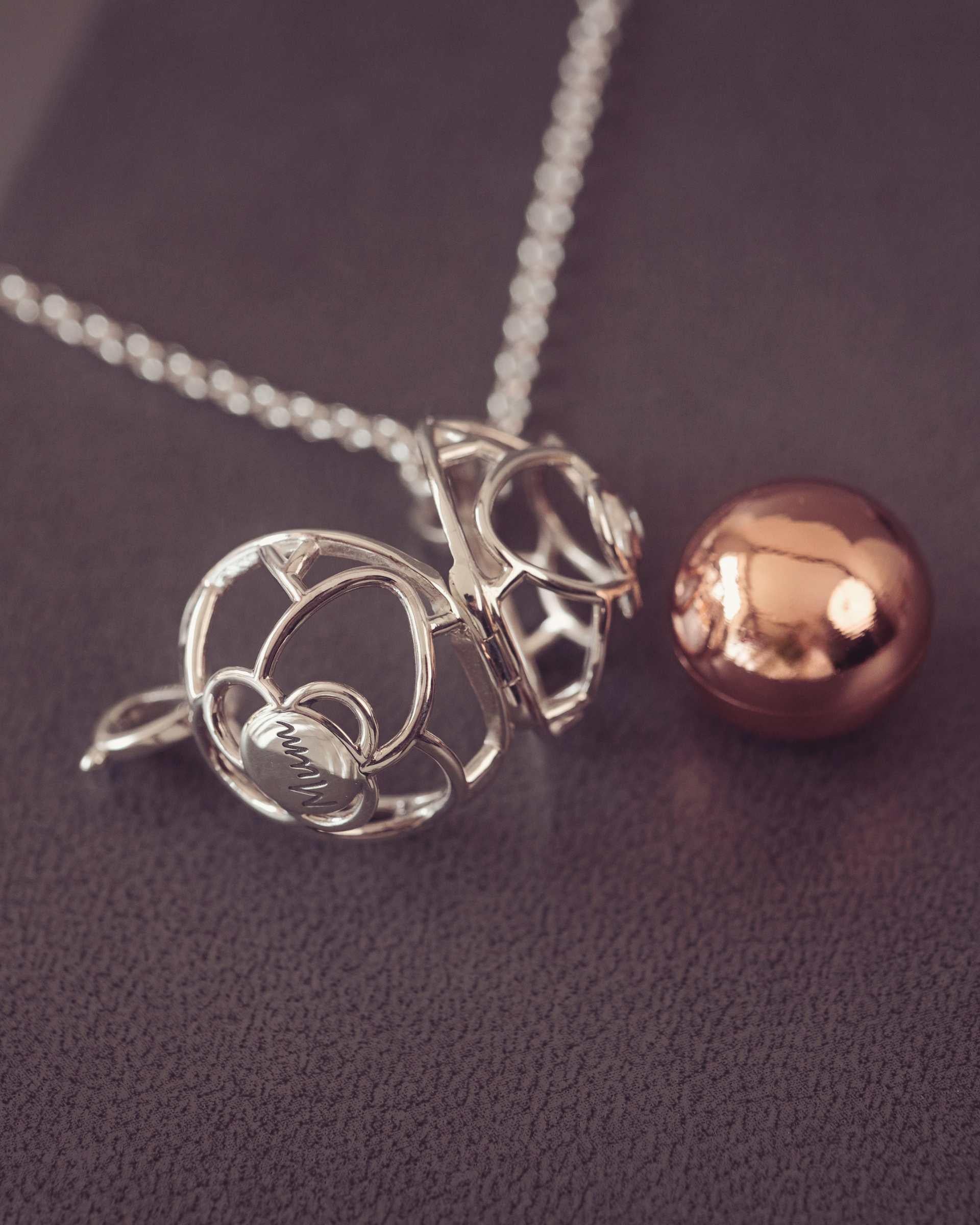 Silver pendant and rose gold sphere on a dark fabric background