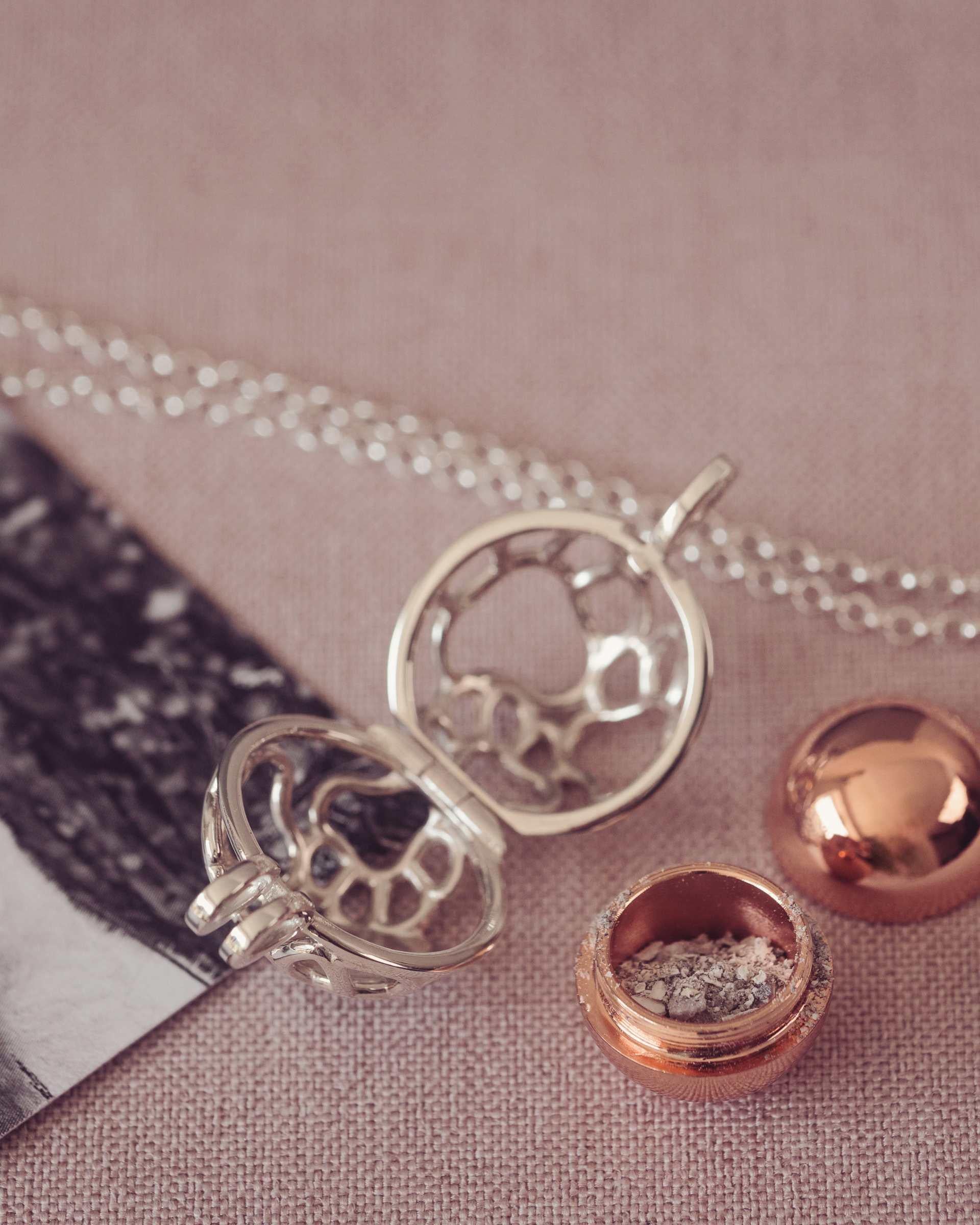 Silver and rose gold necklace with a round locket containing ashes on pink surface.