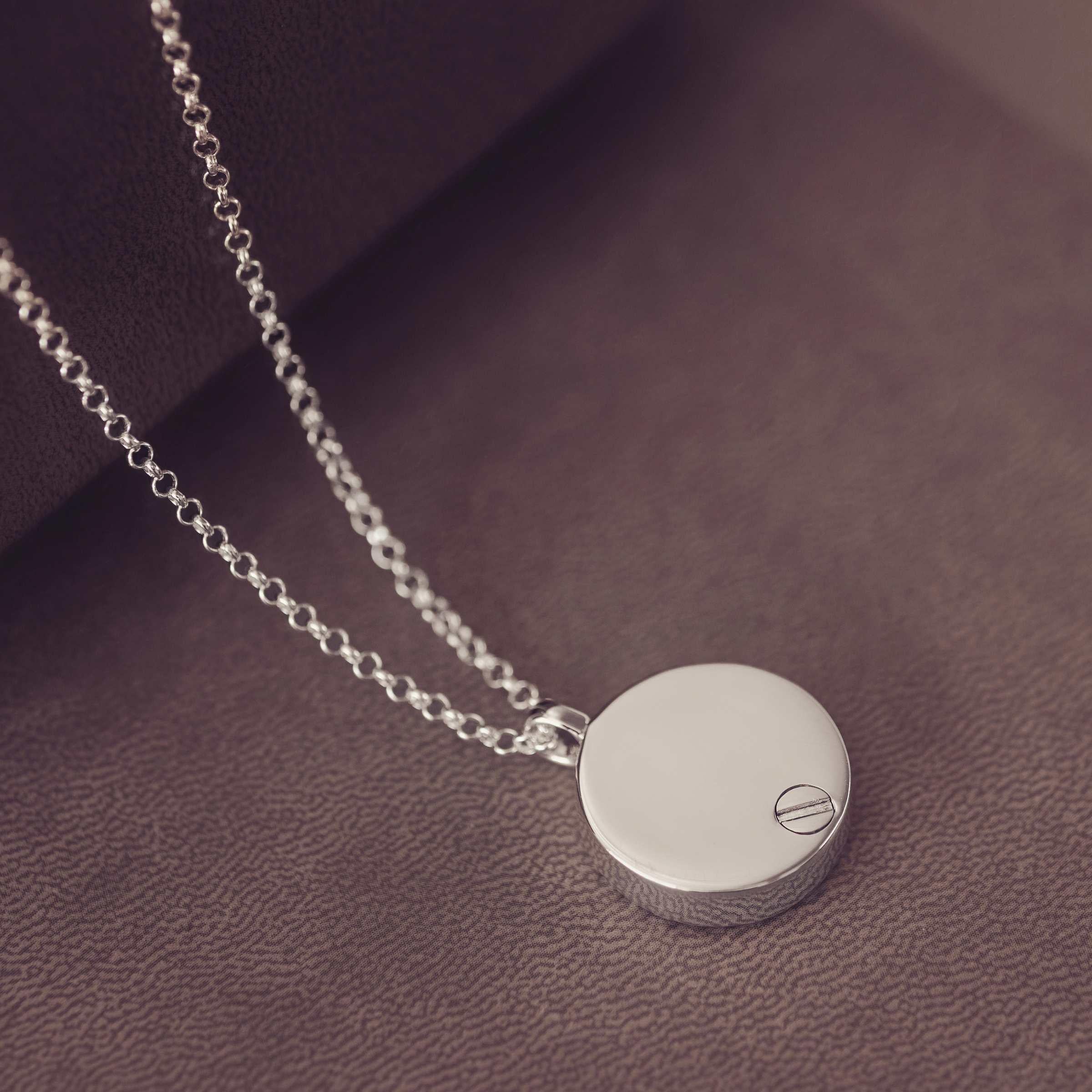 Silver necklace with a round urn pendant on a dark brown surface