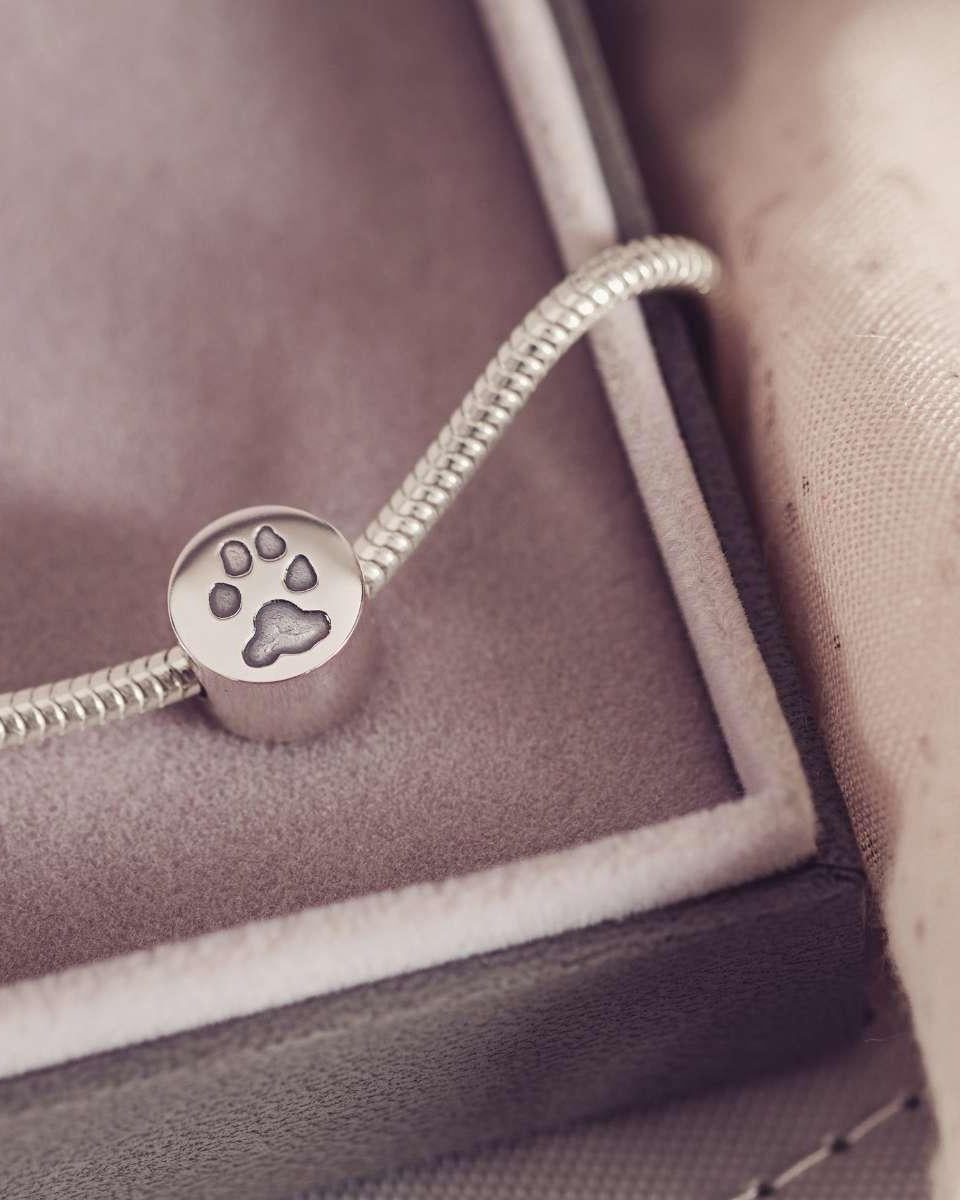 Silver bracelet with a paw print charm on a soft fabric background