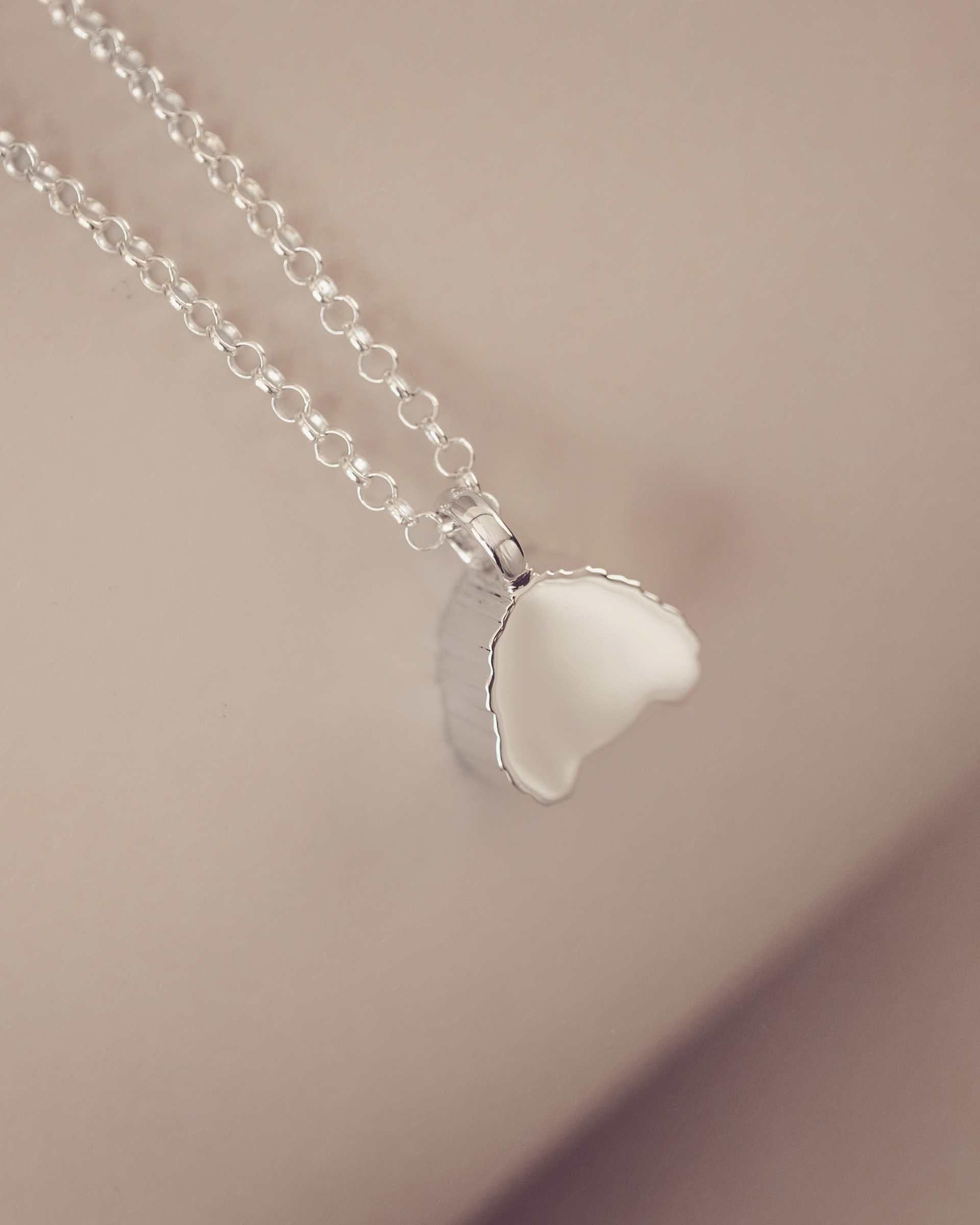 Silver necklace showing a plain blank side on a soft pink background