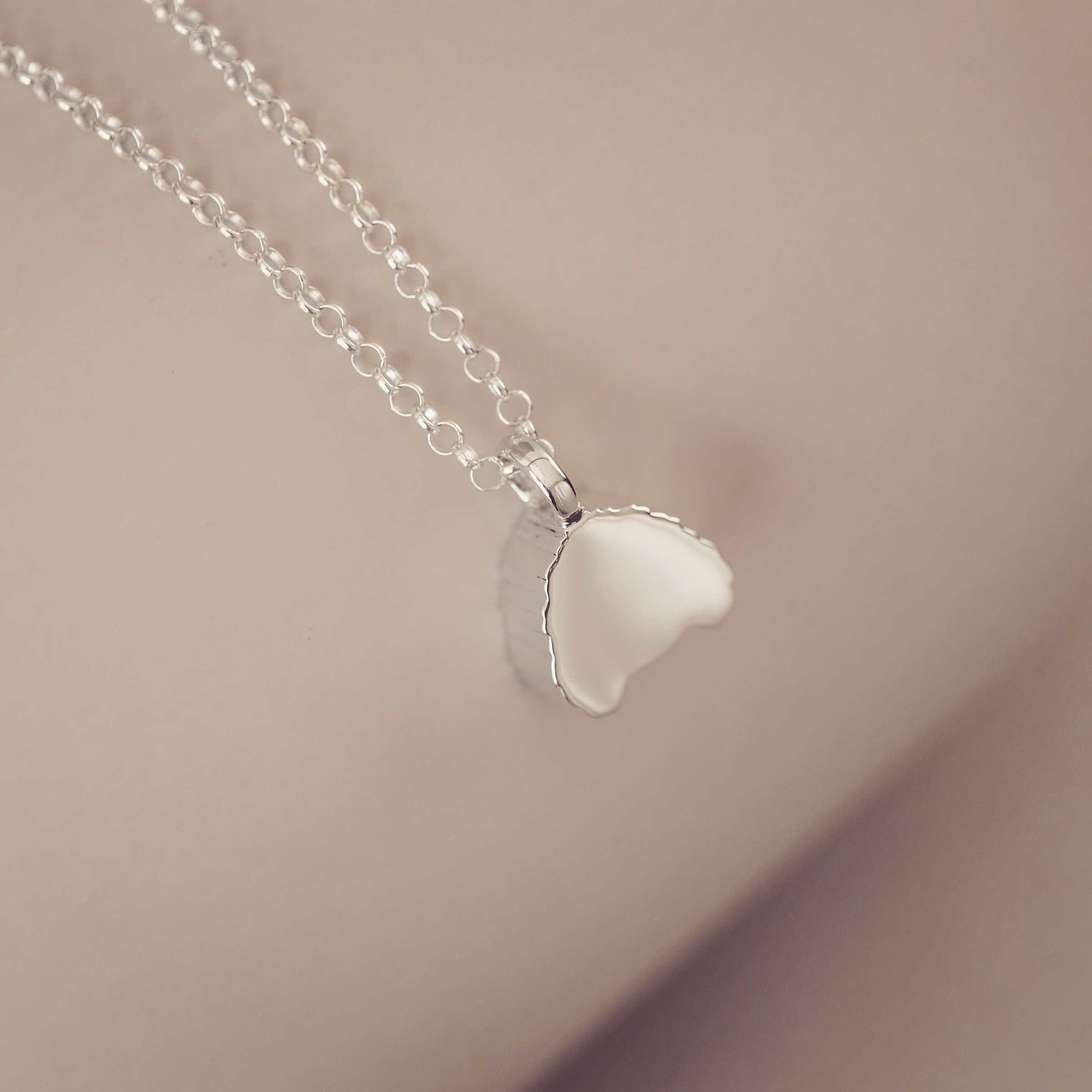Silver necklace showing a plain blank side on a soft pink background