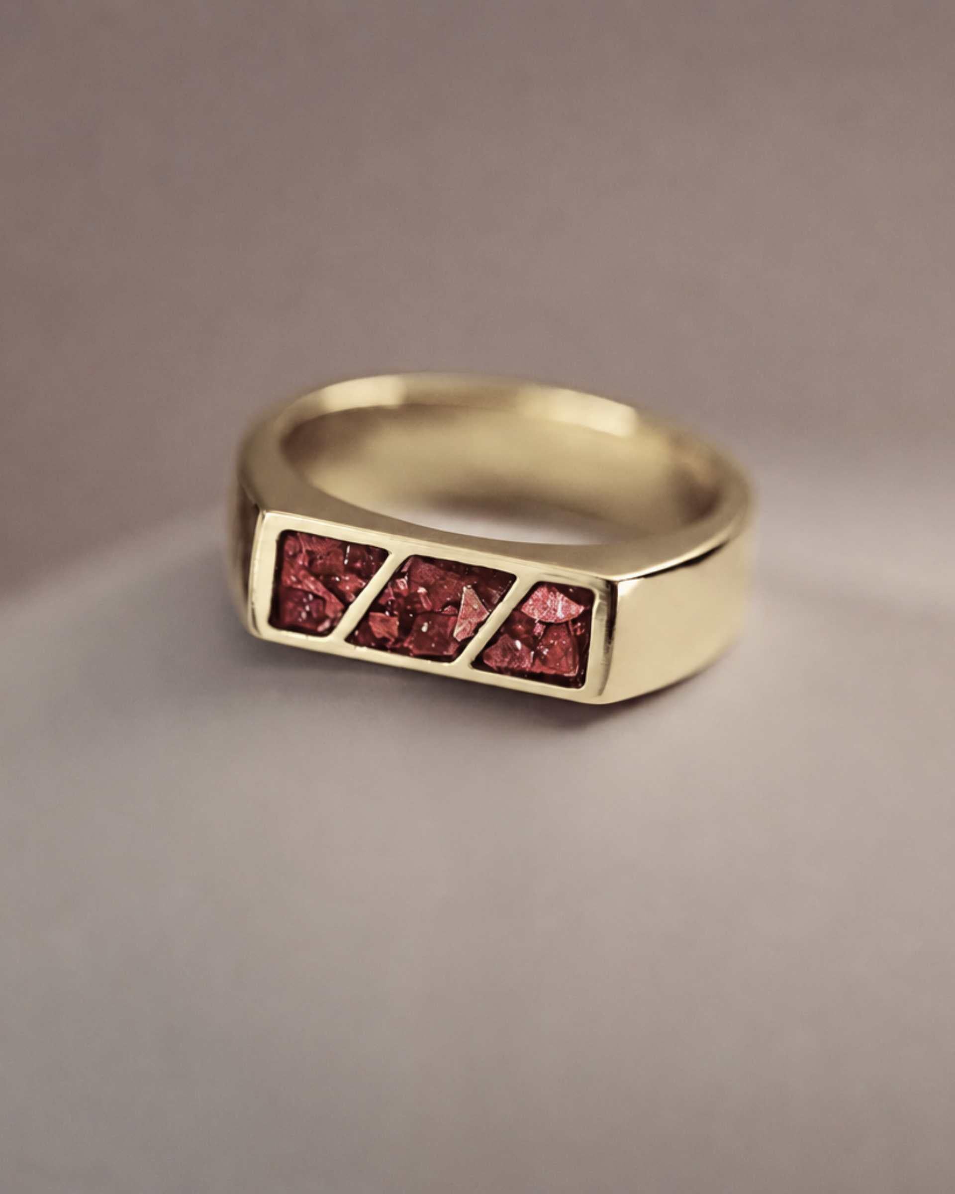 A gold ring with 3 sections of red resin across the top. Sitting on a light background