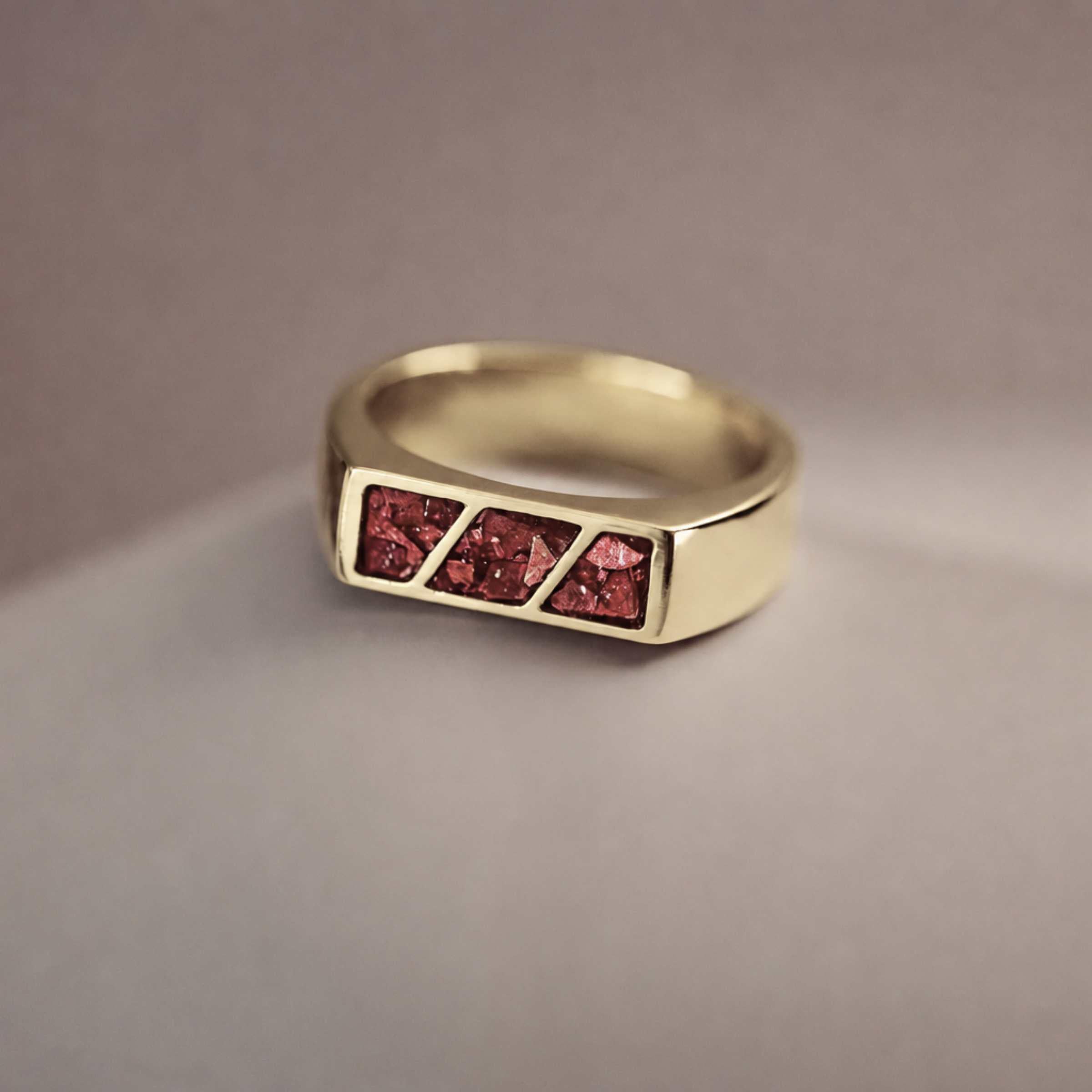A gold ring with 3 sections of red resin across the top. Sitting on a light background