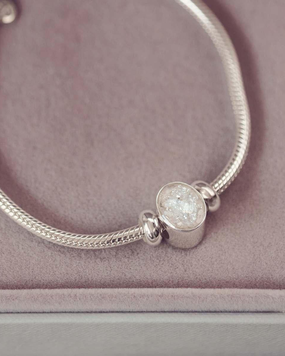 Silver bracelet with a round, textured charm on a pink surface