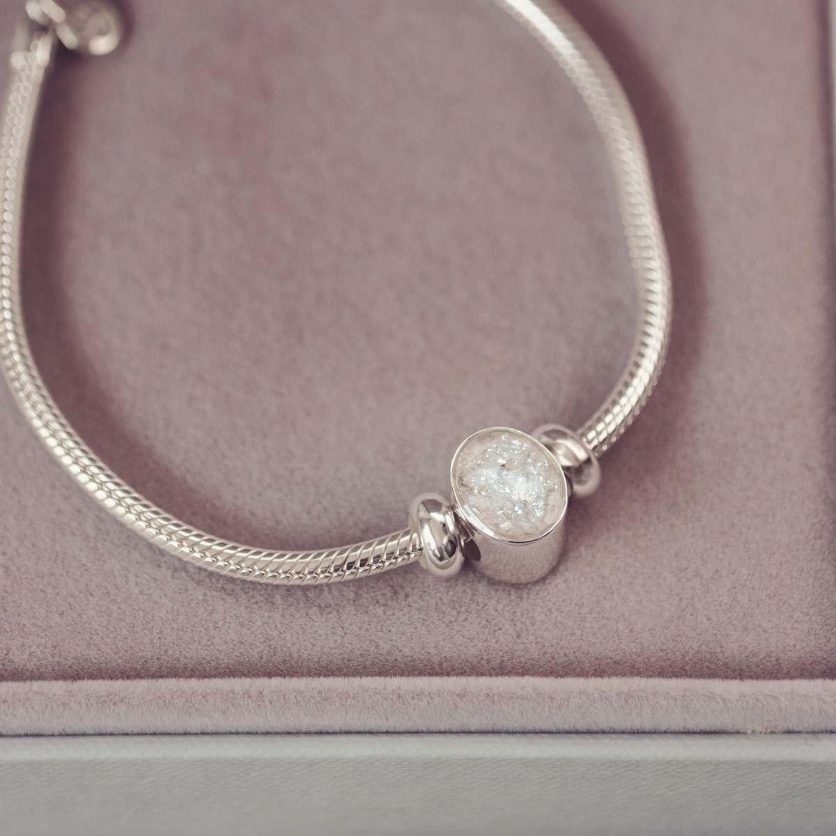 Silver bracelet with a round, textured charm on a pink surface