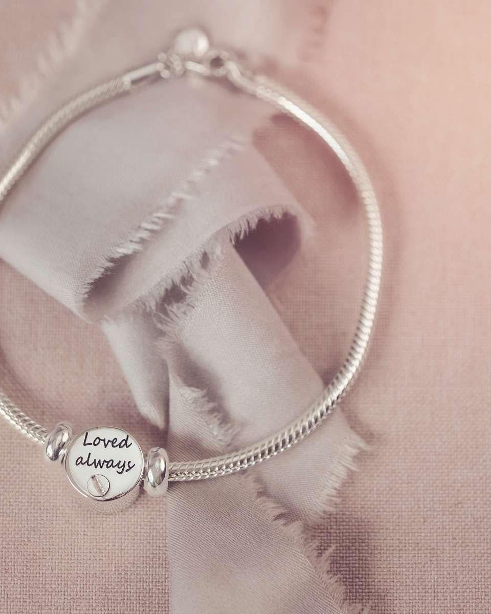 Silver bracelet with a round charm on a soft pink fabric background