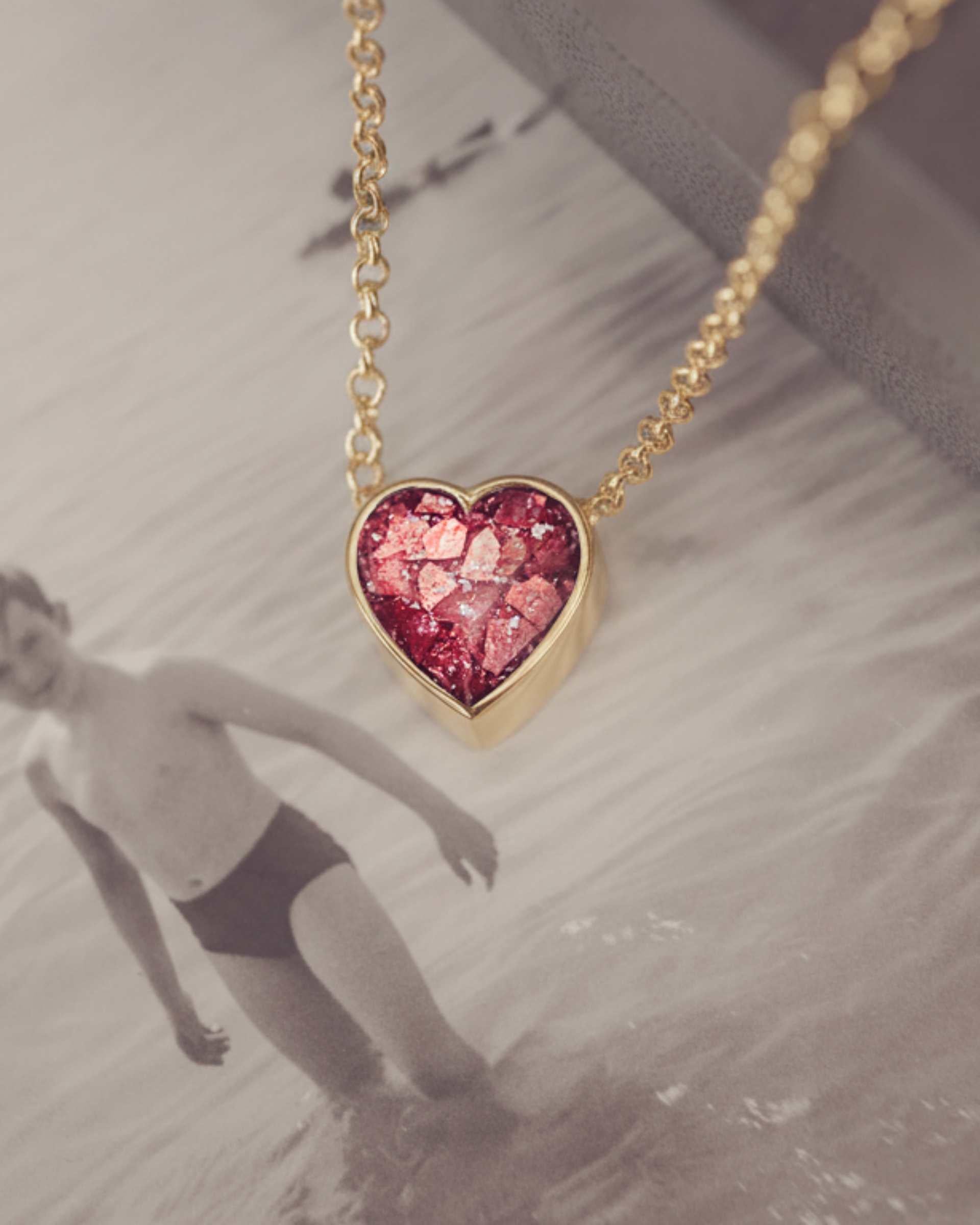 Heart-shaped red necklace on a gold chain with a blurred photograph background